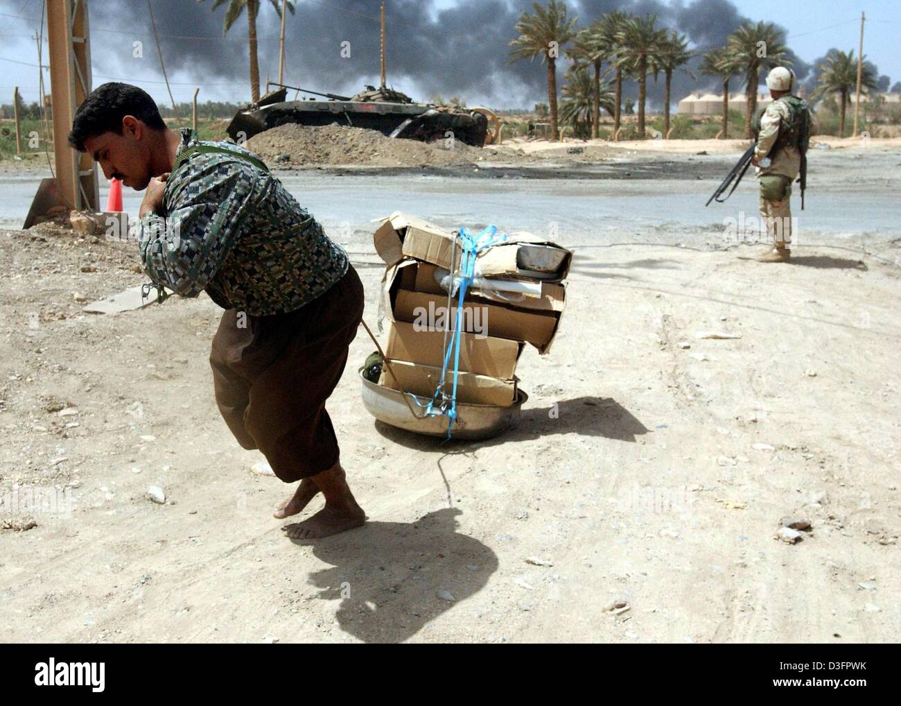 (Afp) - Un Irakien nu tire derrière lui un tas d'articles ménagers pillés au-delà d'un Marine américain qui monte la garde dans une rue de Bagdad, 10 avril 2003. Après la chute de Bagdad, il n'y a que peu d'échanges de tirs dans la capitale, mais de nombreux pillages. Banque D'Images