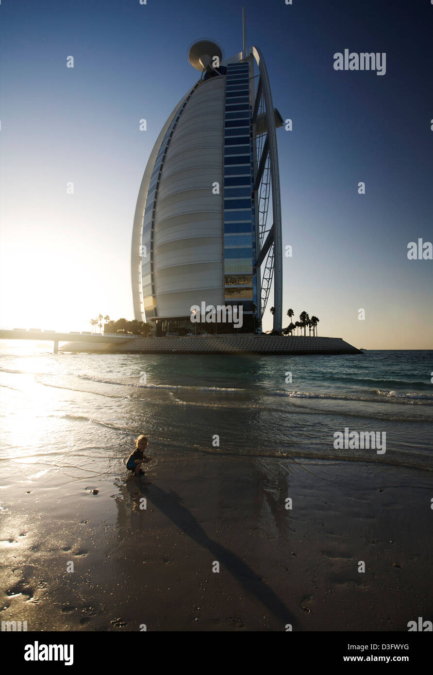 Petit garçon joue sur la plage au coucher du soleil en face de la 7 étoiles hôtel Burj Al Arab à Dubaï aux Émirats arabes unis. C'est le seul hôtel 7*. Banque D'Images