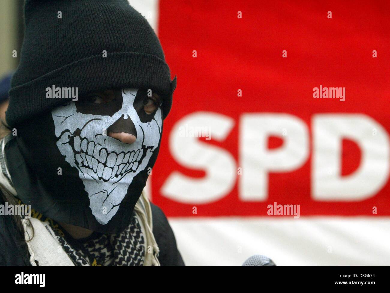 (Afp) - un manifestant se place en avant du SPD logo et porte un masque avec une godille peint sur elle lors d'un rassemblement devant le lieu où le leadership du parti SPD tient une réunion à Bochum, Allemagne, 16 novembre 2003. La direction du parti s'est réuni afin de préparer le congrès du parti SPD. Environ 150 manifestants s'étaient réunis devant le lieu et se sont mobilisés contre les gouvernements r Banque D'Images