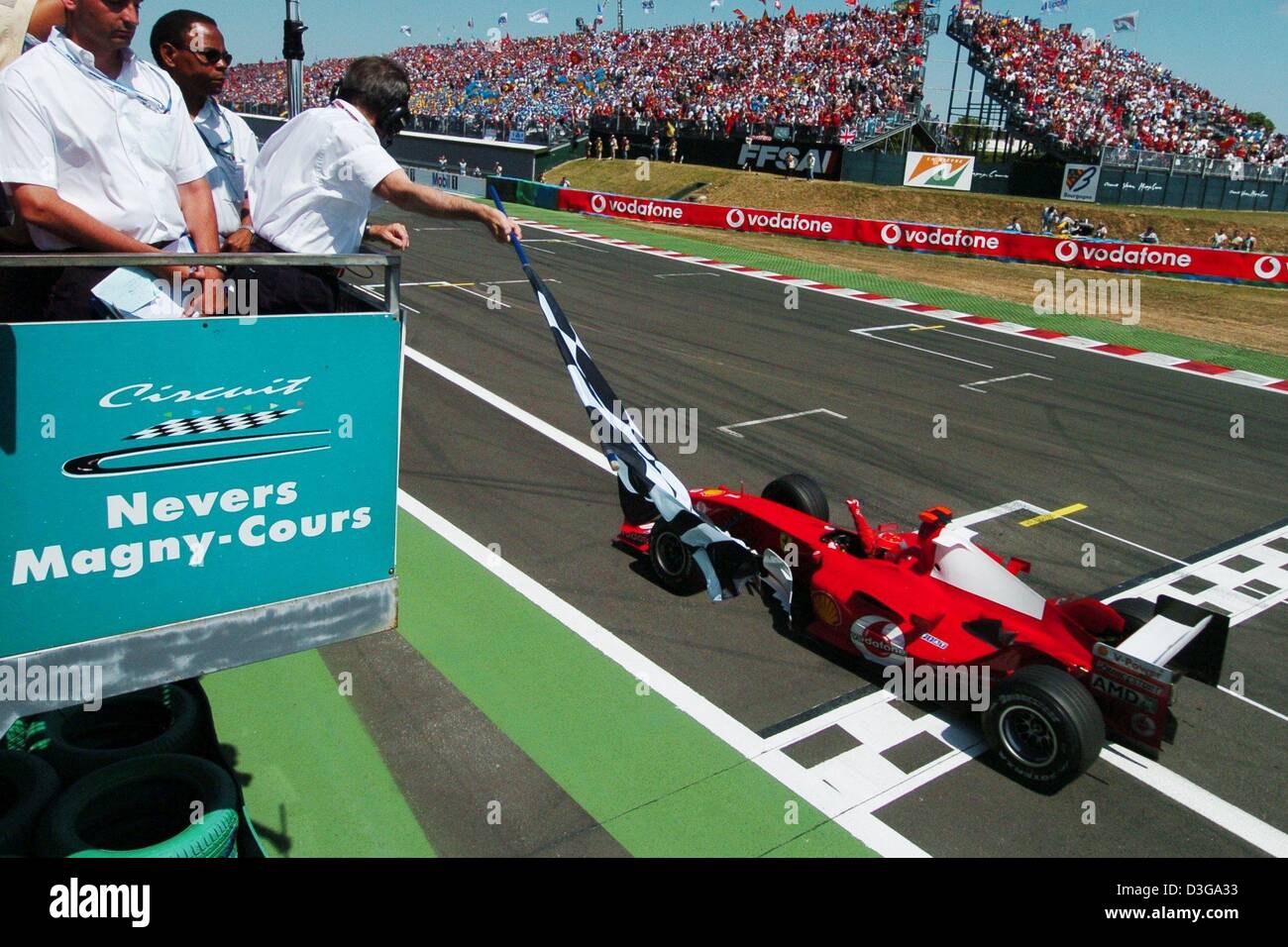 (Afp) - L'Allemand Michael Schumacher, pilote de formule 1 de Ferrari à la vôtre comme il conduit sa voiture de course passé le checkered flagg de franchir la ligne d'arrivée à la fin de la Grand Prix de France à Magny-Cours, France, 4 juillet 2004. Schumacher a remporté la course et a réussi à accroître son avance à 90 points dans le classement global. Banque D'Images