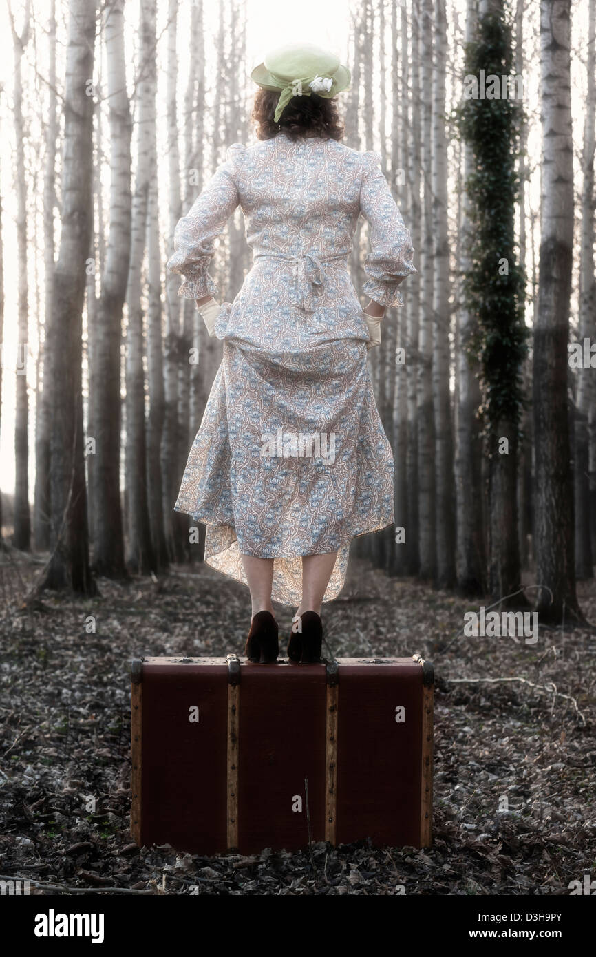 Une femme dans une robe vintage floral est debout sur une vieille valise Banque D'Images