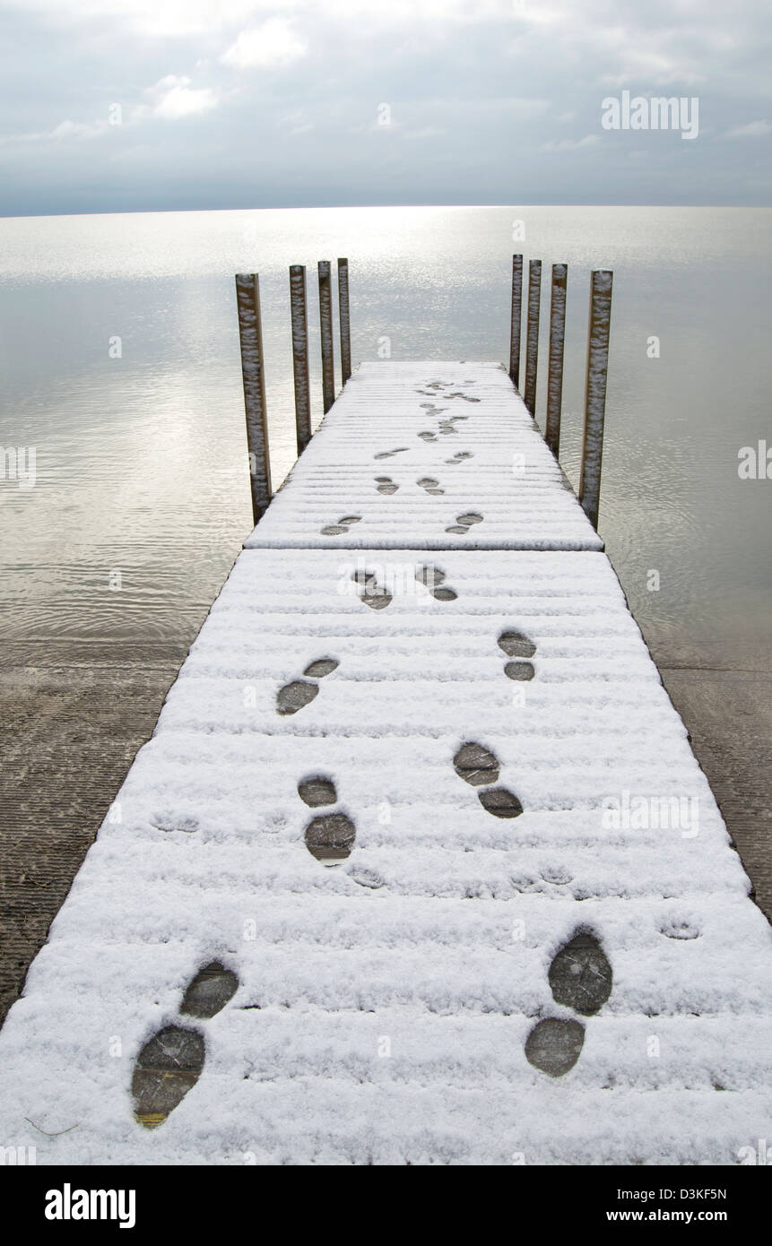 Les traces de pas dans la neige sur un quai menant dehors et à l'arrière, sur un grand lac. Banque D'Images