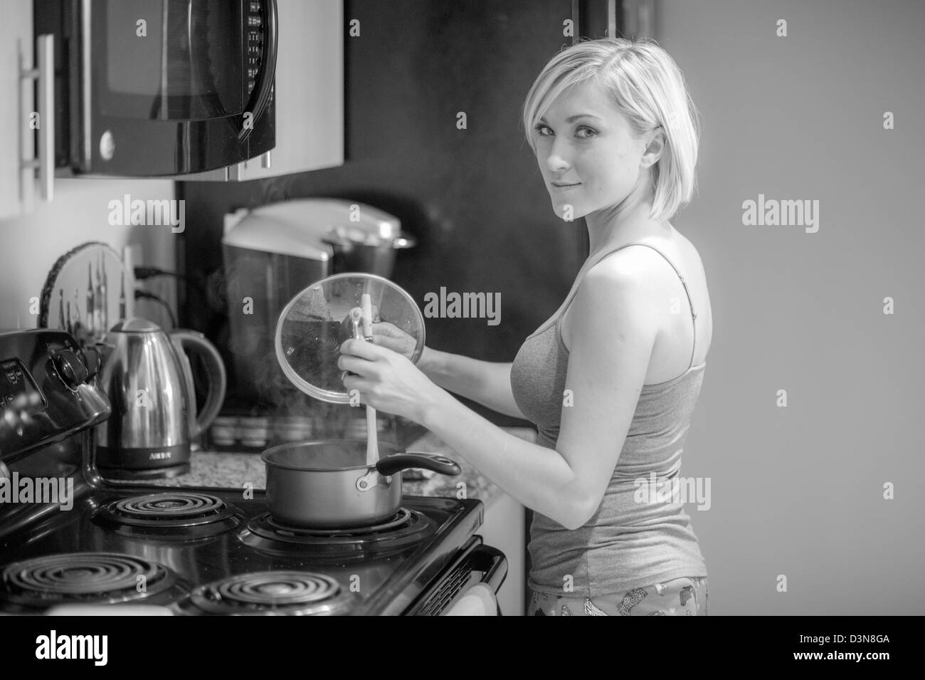 Jeune blonde woman cooking in kitchen Banque D'Images