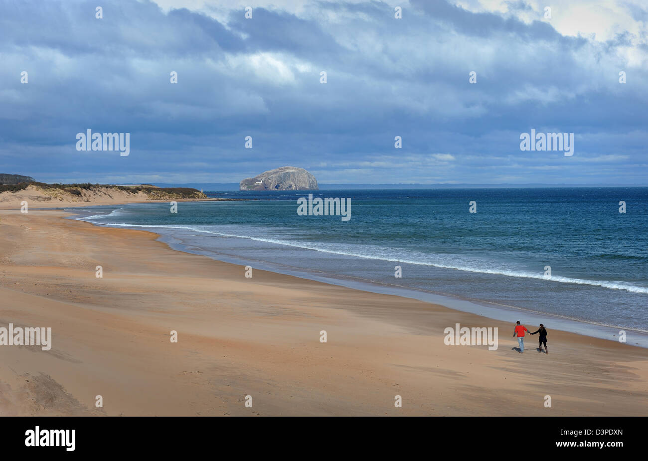 Un couple marche sur le long de la plage déserte Tyningham vers la Bass Rock dans la distance, North Berwick, en Écosse. Banque D'Images