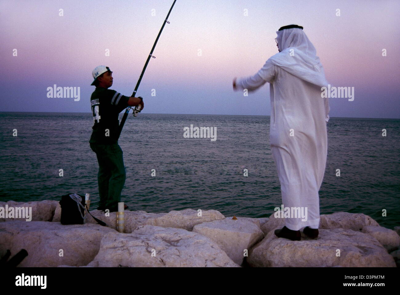 Un Saoudien s'entretient avec un ressortissant de pays tiers tandis que la pêche sur son temps de loisir comme les couchers de soleil sur le golfe Persique à Al Khobar. Banque D'Images