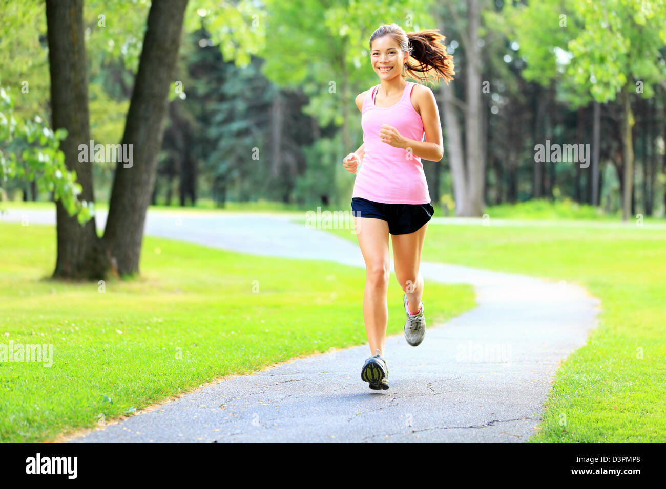 Happy Asian / Caucasian woman running in park sur journée d'été, avec du soleil dans les arbres verts Banque D'Images