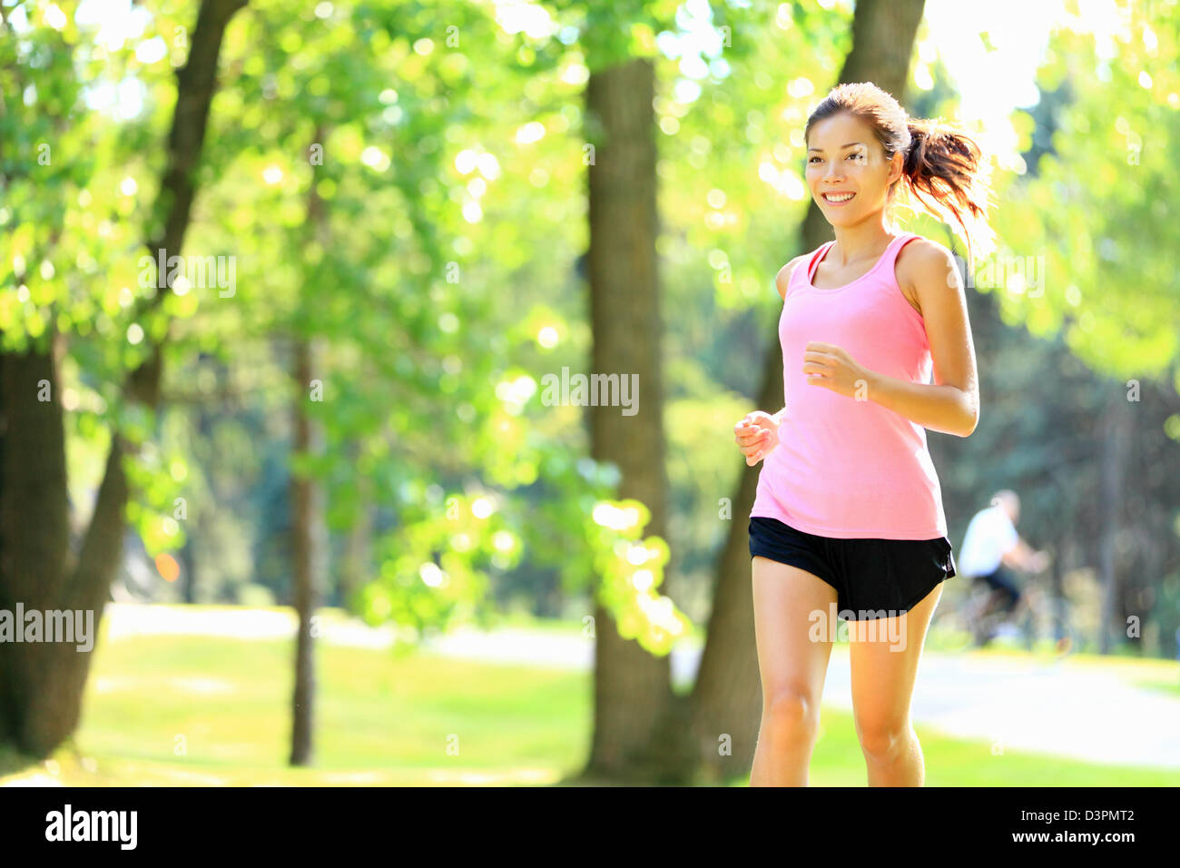 Happy Asian / Caucasian woman running in Park City aux beaux jours avec du soleil dans les arbres verts Banque D'Images