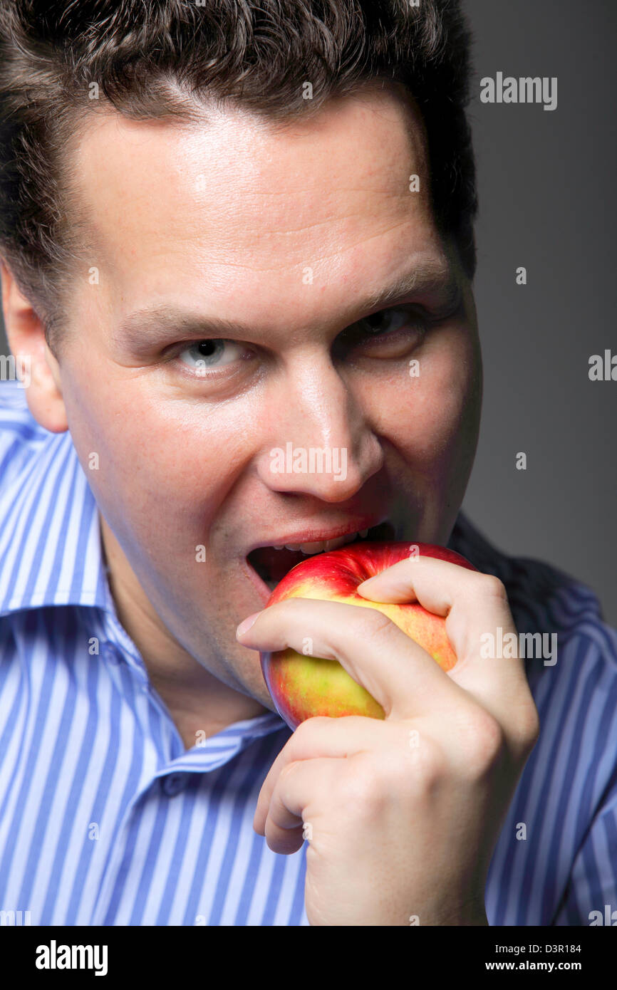 Portrait d'un homme mûr sur le point de manger une pomme rouge fond gris Banque D'Images