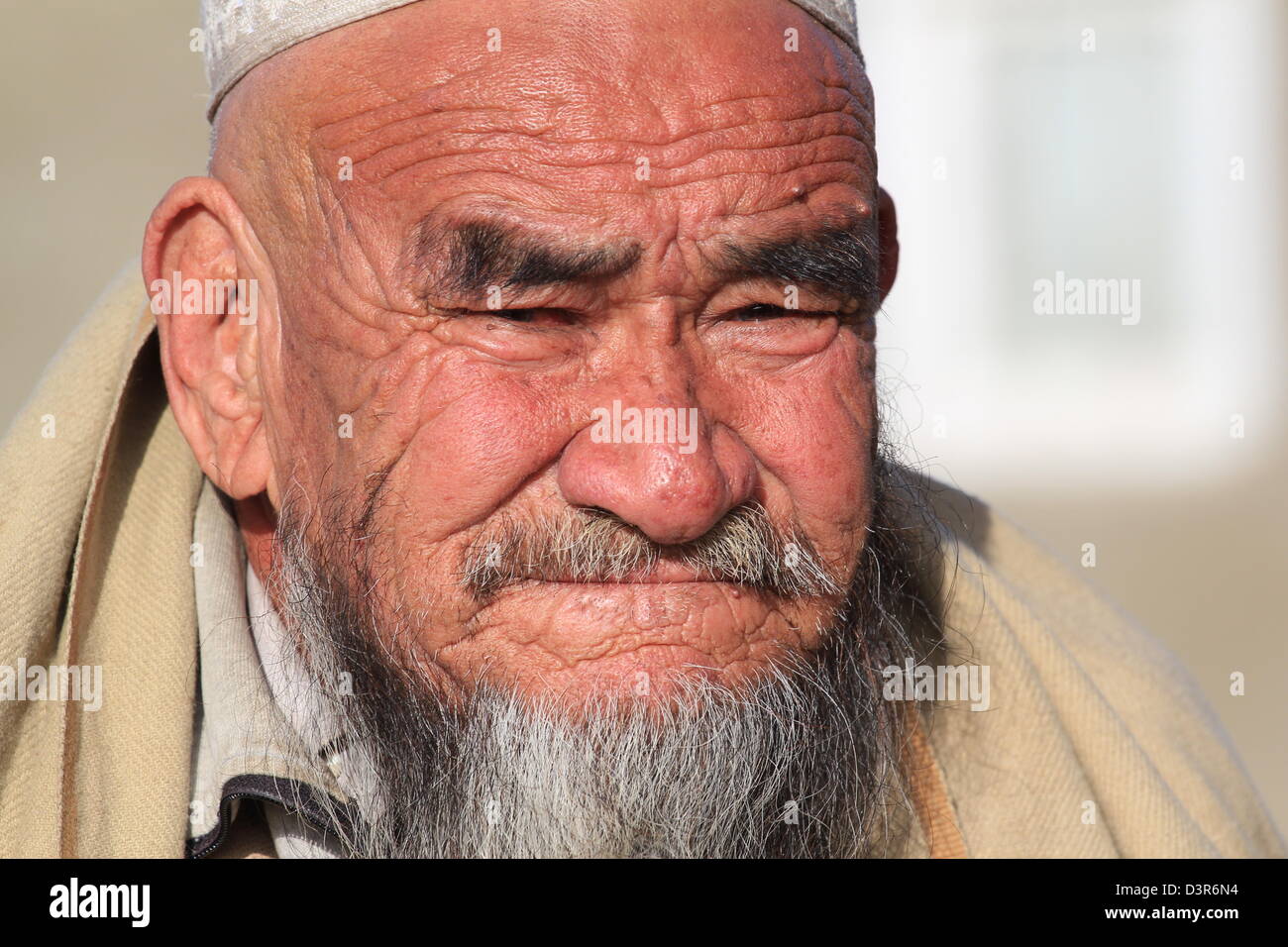 Un vieil homme est assis sur un mur à Kaboul. Son visage montre bordée d'années avancée et ses yeux loucher pour voir à travers la lumière du soleil. Banque D'Images