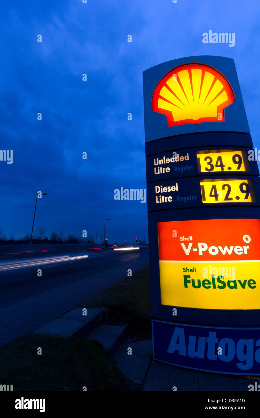 Prix du carburant Shell signe éclairés la nuit. Voitures qui passent sur la route aux côtés de quitter les sentiers de lumière. Banque D'Images
