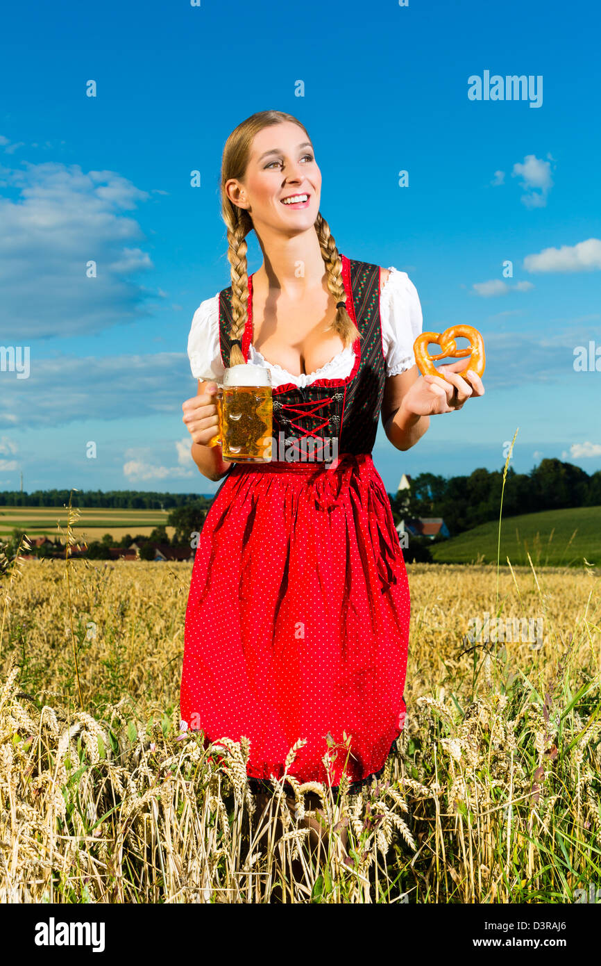 Jeune femme à boire la bière bavaroise et en gardant un bretzel dans dirndl à Meadow Banque D'Images