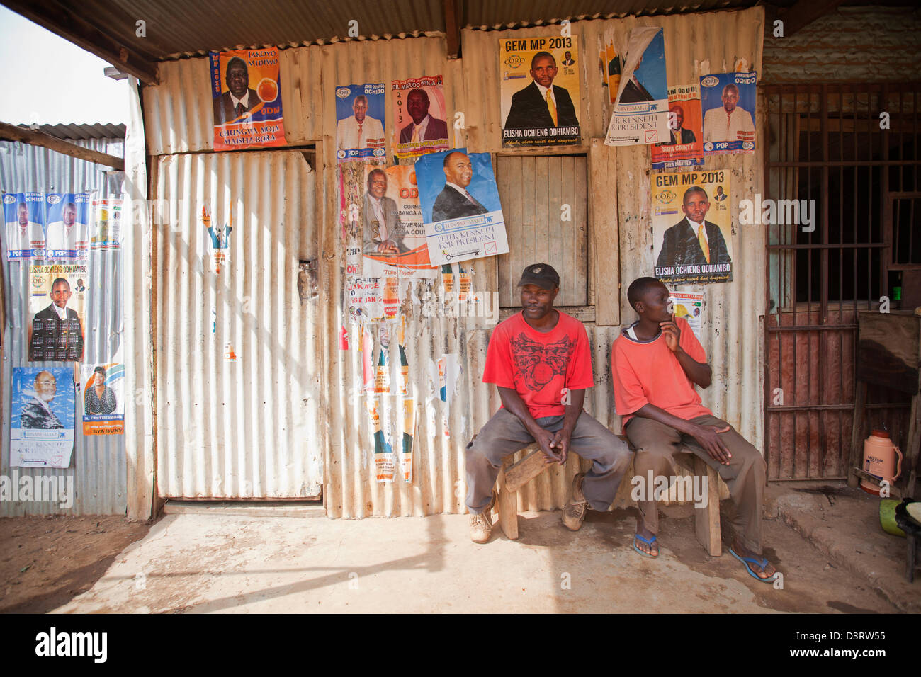 Les hommes assis en face de l'atelier fermé couvert d'affiches politiques, Yala, Province de Nyanza, au Kenya, en février 2013. Banque D'Images