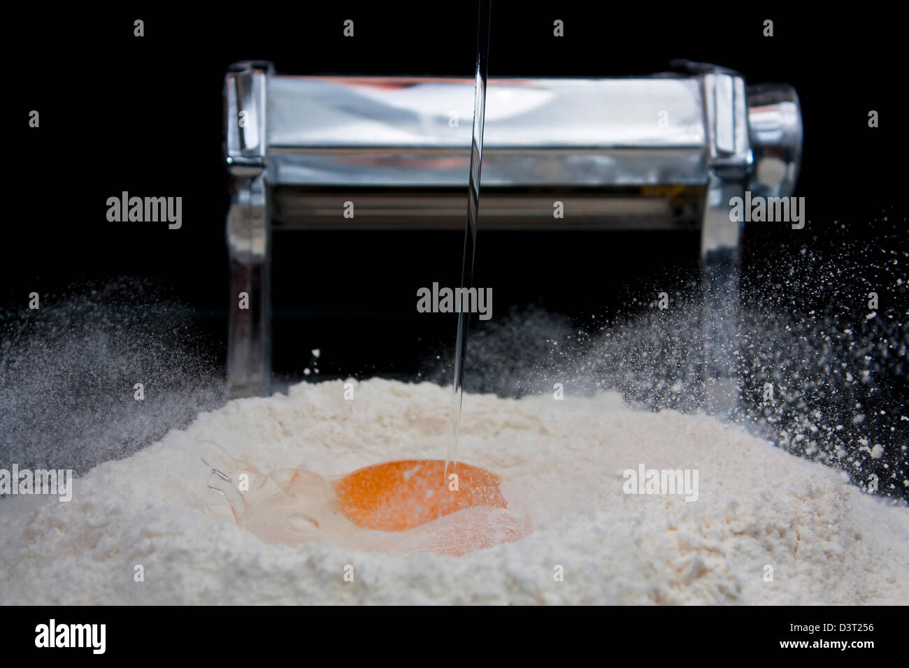 Des œufs frais entrant dans la farine avec une machine à pâtes en arrière-plan Banque D'Images