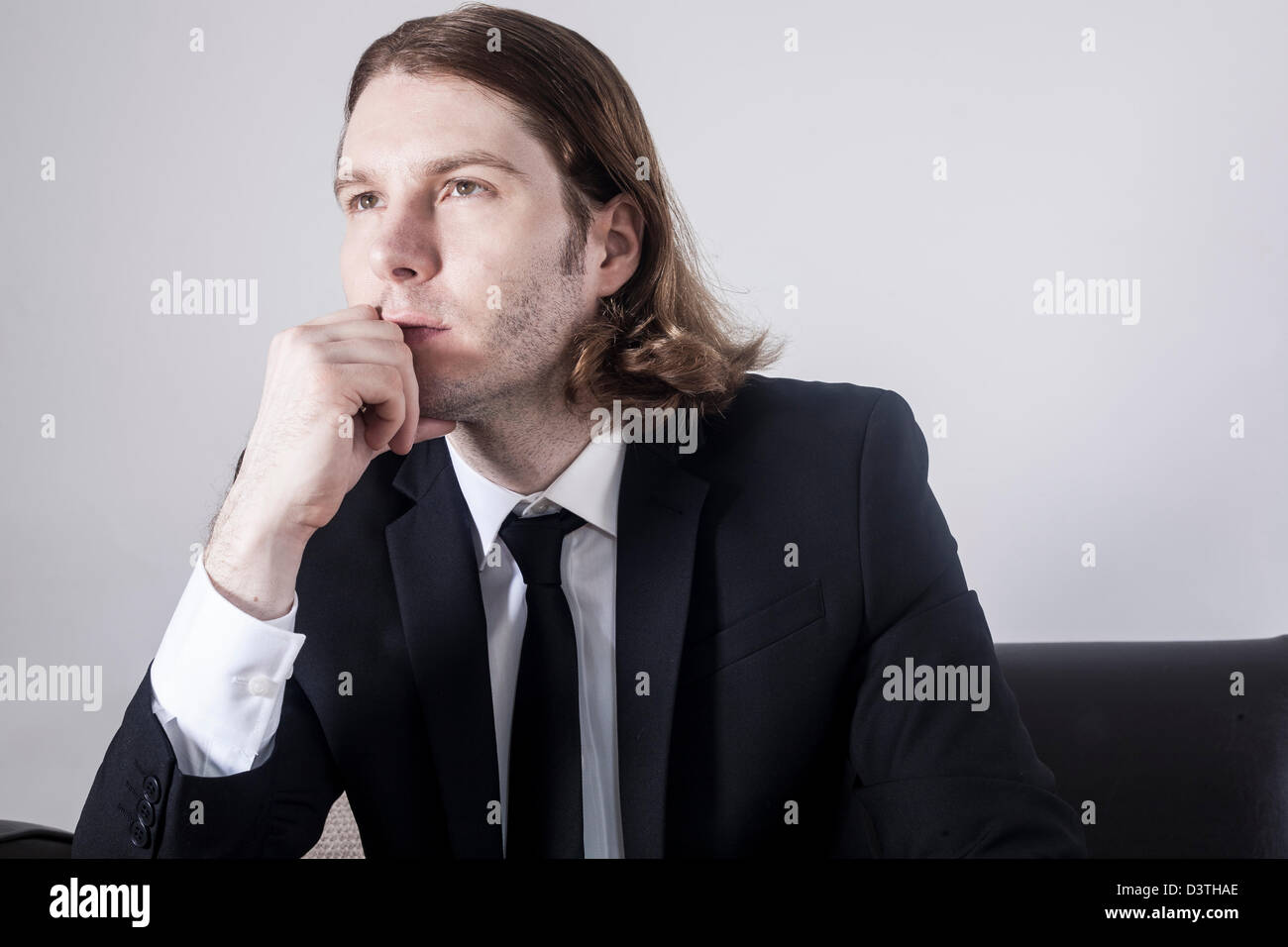 En fonction de l'homme aux cheveux longs assis sur le canapé avec la tête posée sur le menton de penser et à la recherche dans la distance Banque D'Images