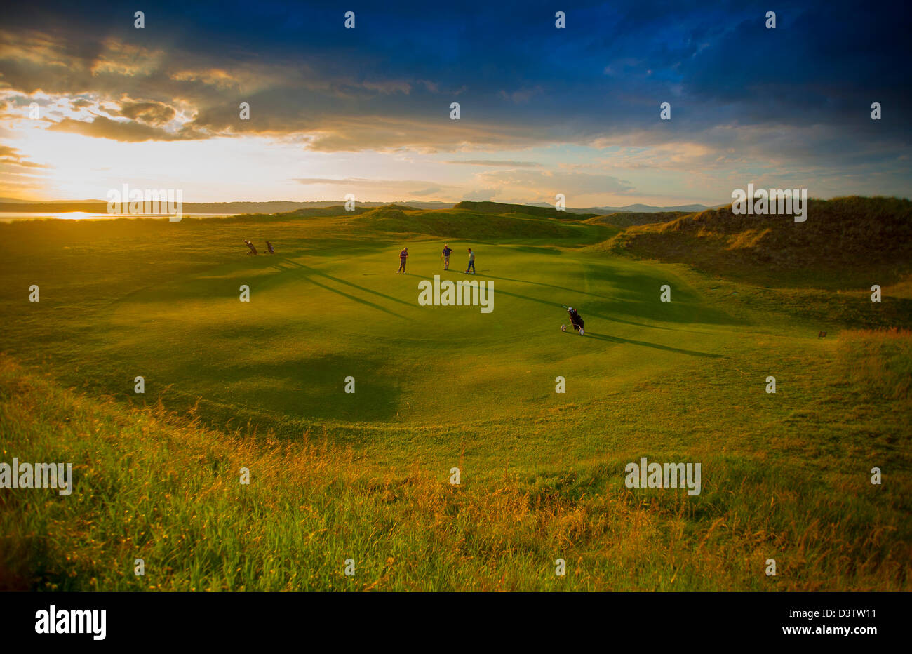 Les golfeurs au coucher du soleil avec des joueurs, mettant de longues ombres sur le parcours de golf et un ciel vert. Banque D'Images