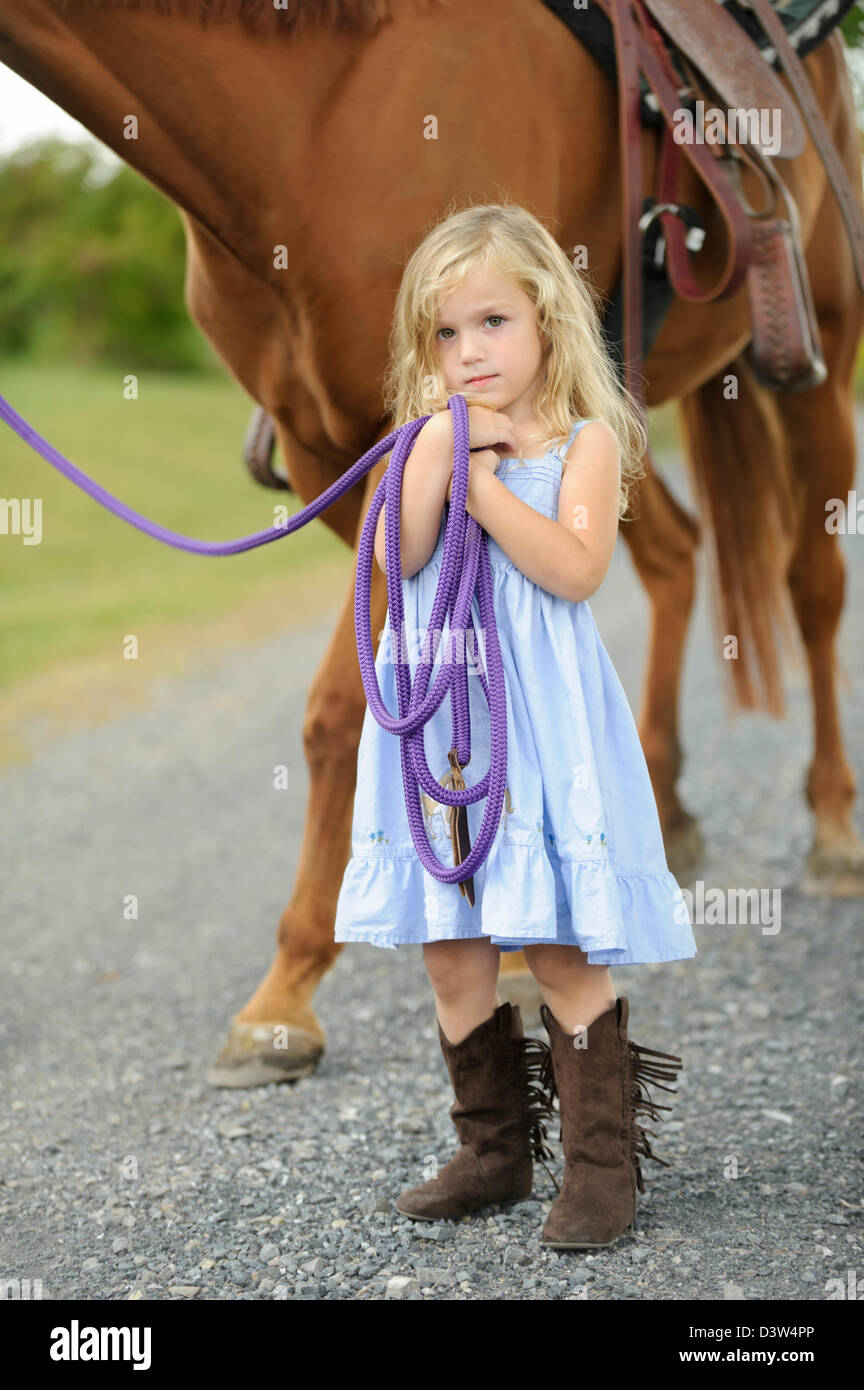 Petite fille blonde debout à côté d'un grand cheval tout en maintenant la ligne de sonde. Banque D'Images