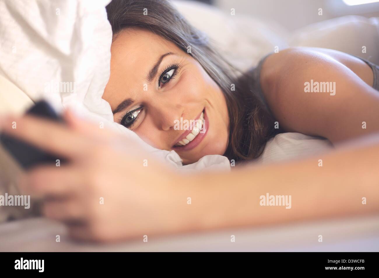 Happy woman lying on bed smiling pendant la lecture d'un message texte à partir de quelqu'un Banque D'Images