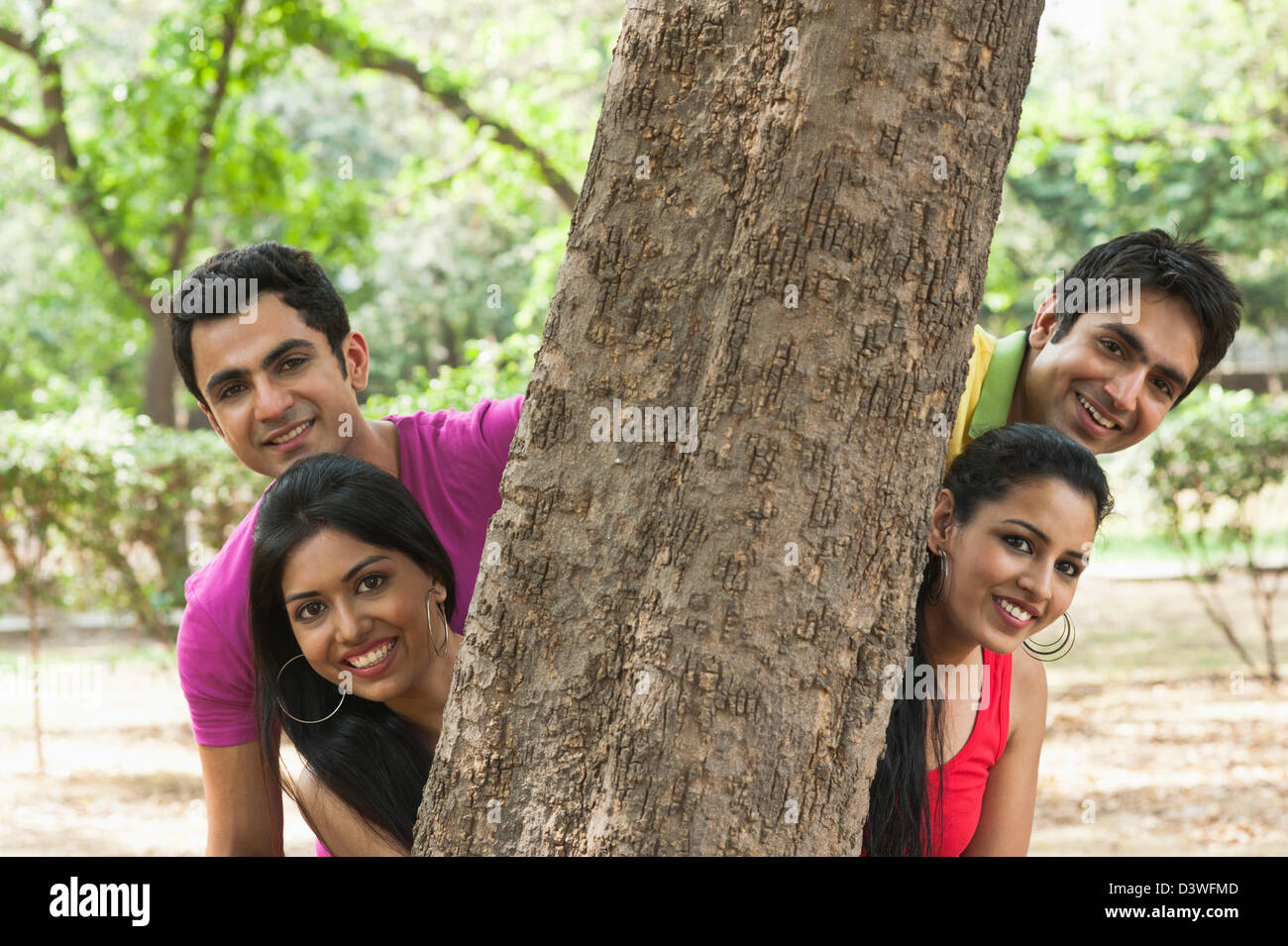 Les amis de se cacher derrière un arbre dans un parc, Lodi Gardens, New Delhi, Delhi, Inde Banque D'Images