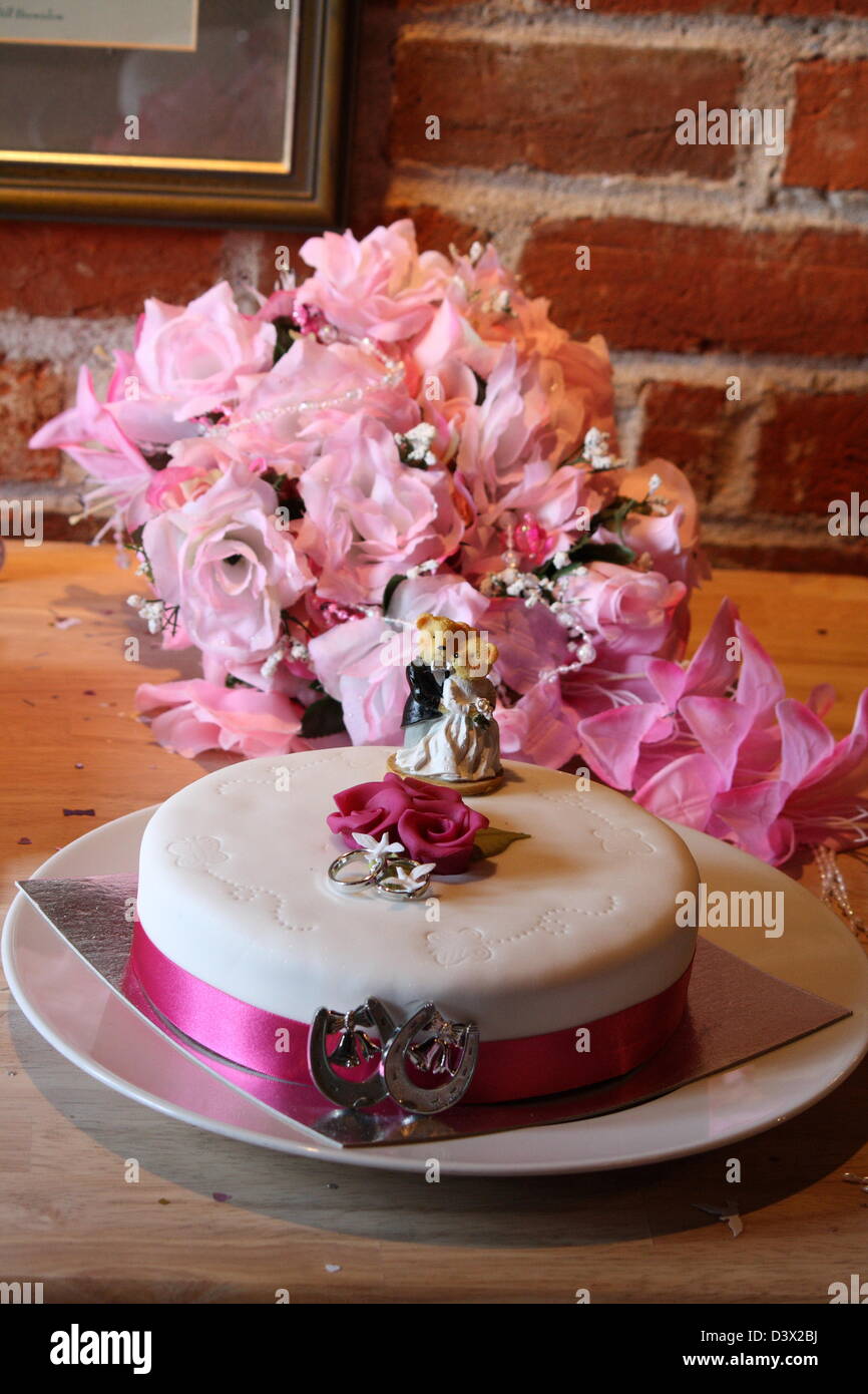 Gâteau de mariage avec deux ours et ruban rose autour d'elle, en face d'un bouquet de fleurs. Banque D'Images