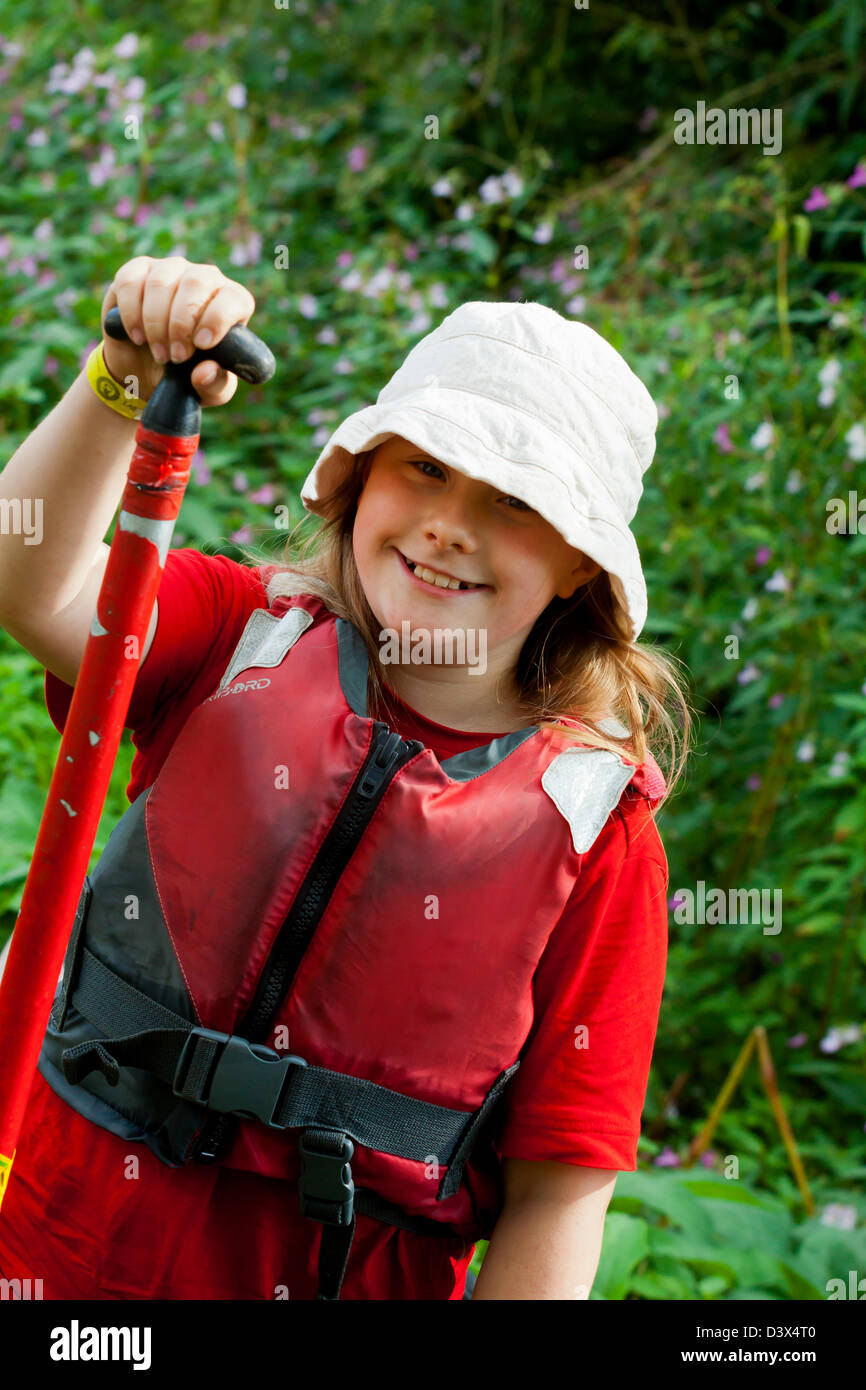 Dans l'enfant gilet rouge portant un chapeau et tenant une pagaie canoë avant dans une rivière Banque D'Images