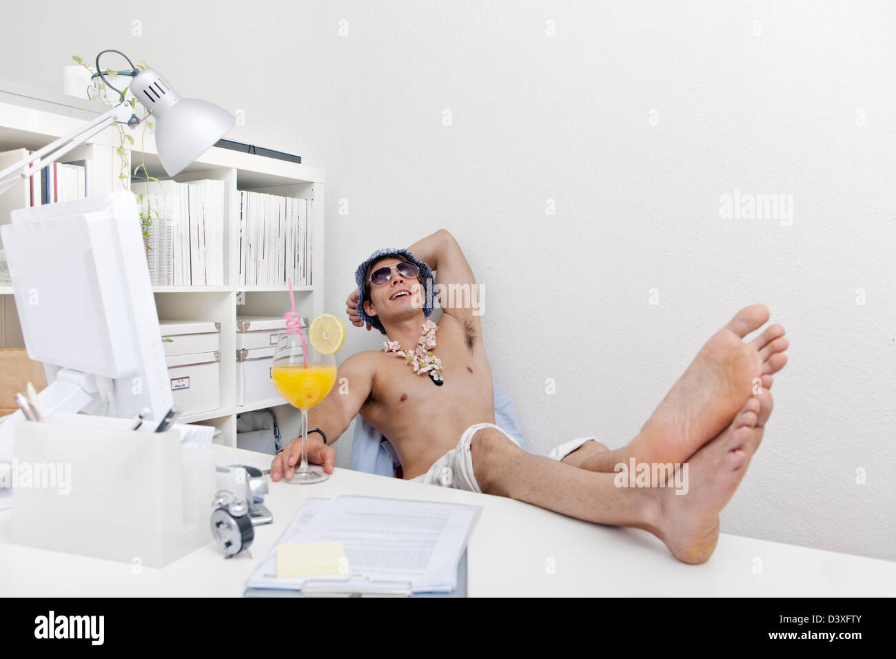 Jeune homme de maillots de bain et des lunettes de soleil et et lei (garland) avec verre à cocktail au travail. Dans l'ambiance vacances. Banque D'Images
