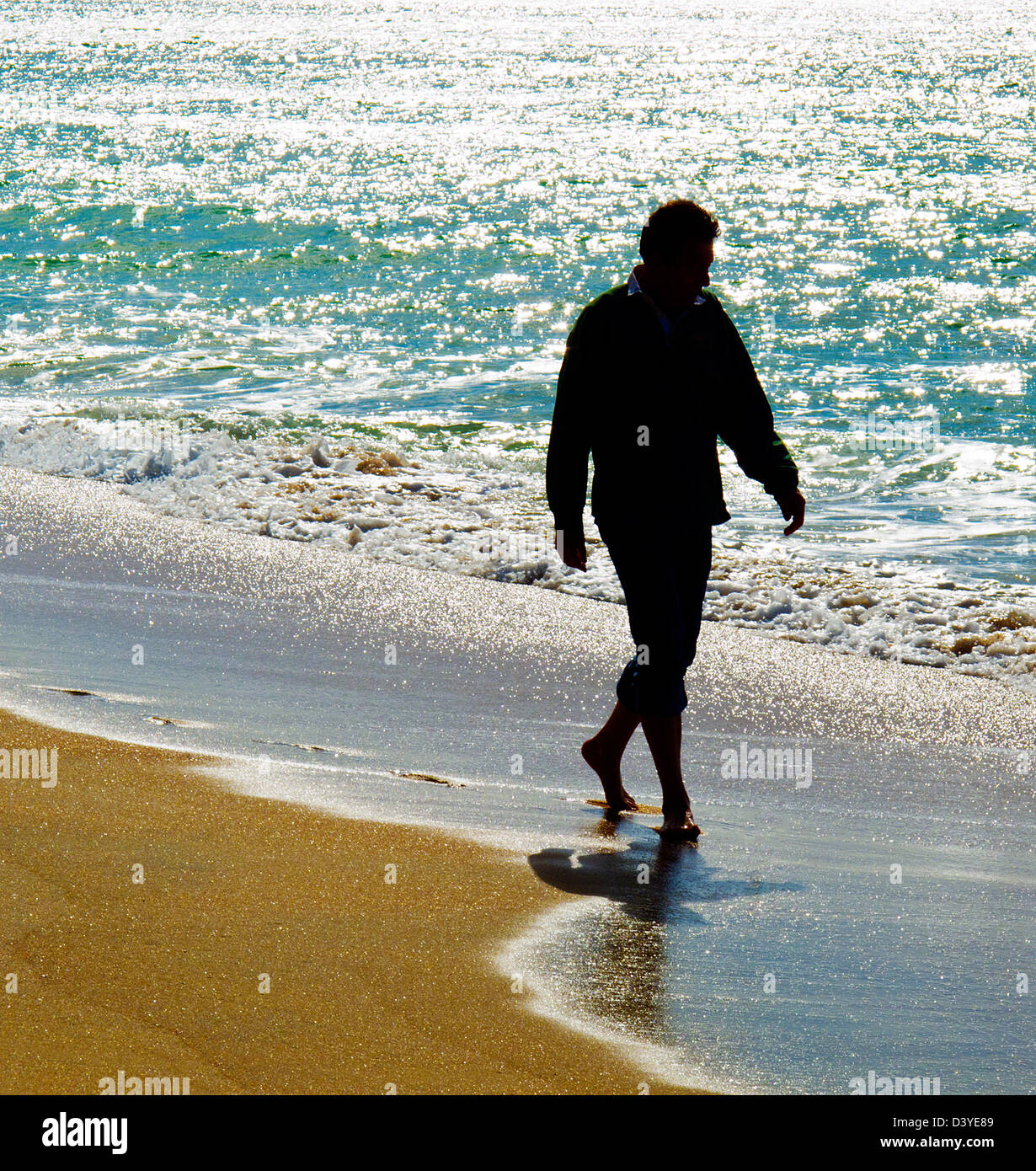 Un homme marche pieds nus le long du rivage d'une plage de sable. Banque D'Images