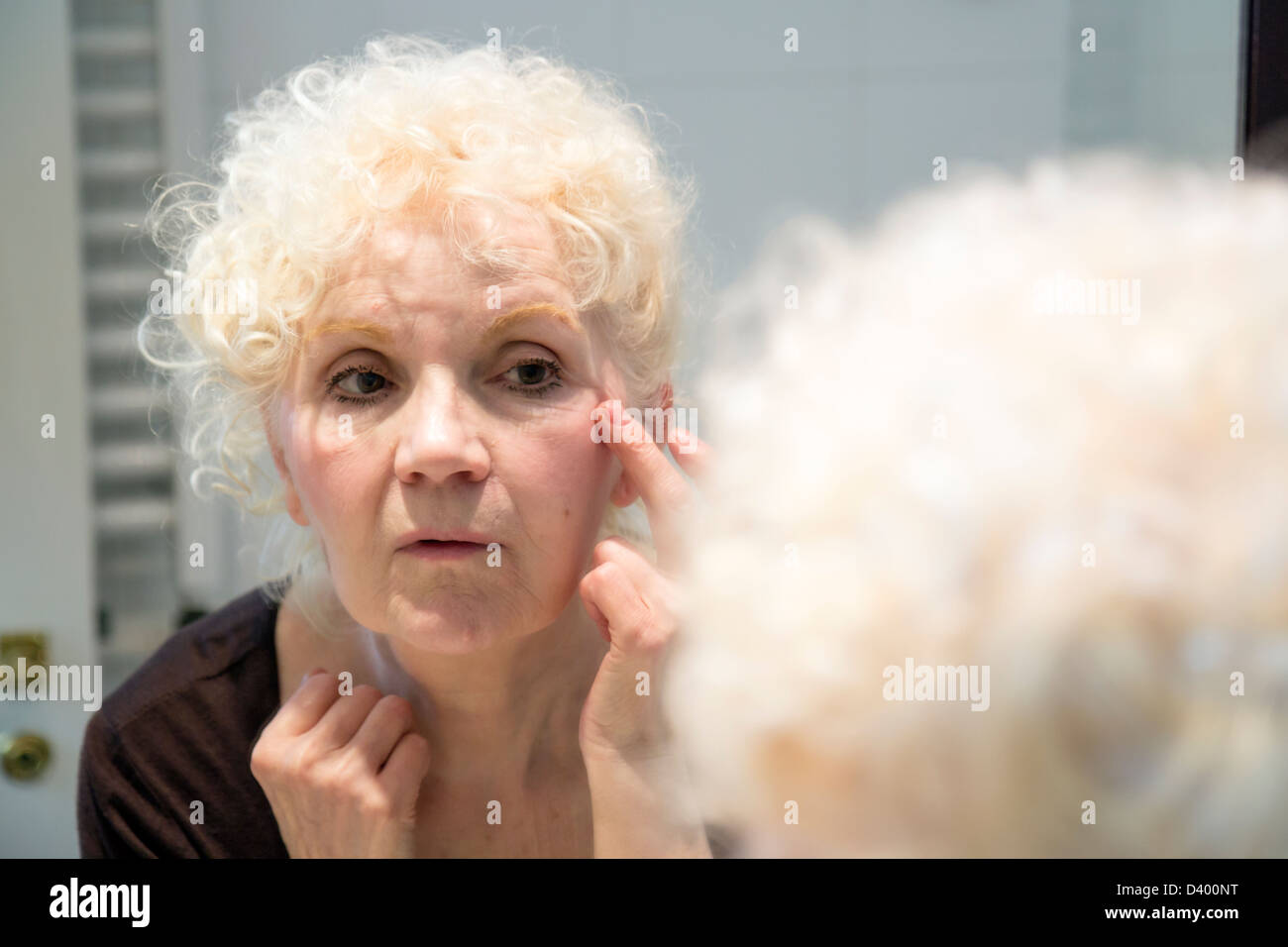 Blonde woman touching her face et à ses rides dans un miroir dans la salle de bains Banque D'Images