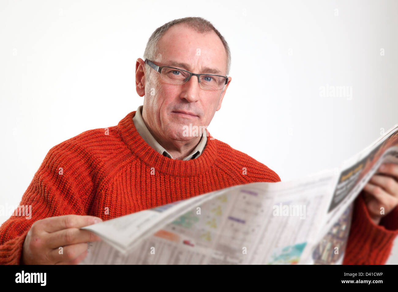 Homme mûr en 50s le port de chandail, la lecture d'un journal grand format, à la caméra à grave. Banque D'Images