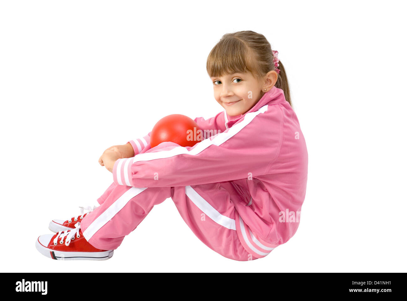 La petite fille dans un costume de sport rose siège avec une boule rouge Banque D'Images