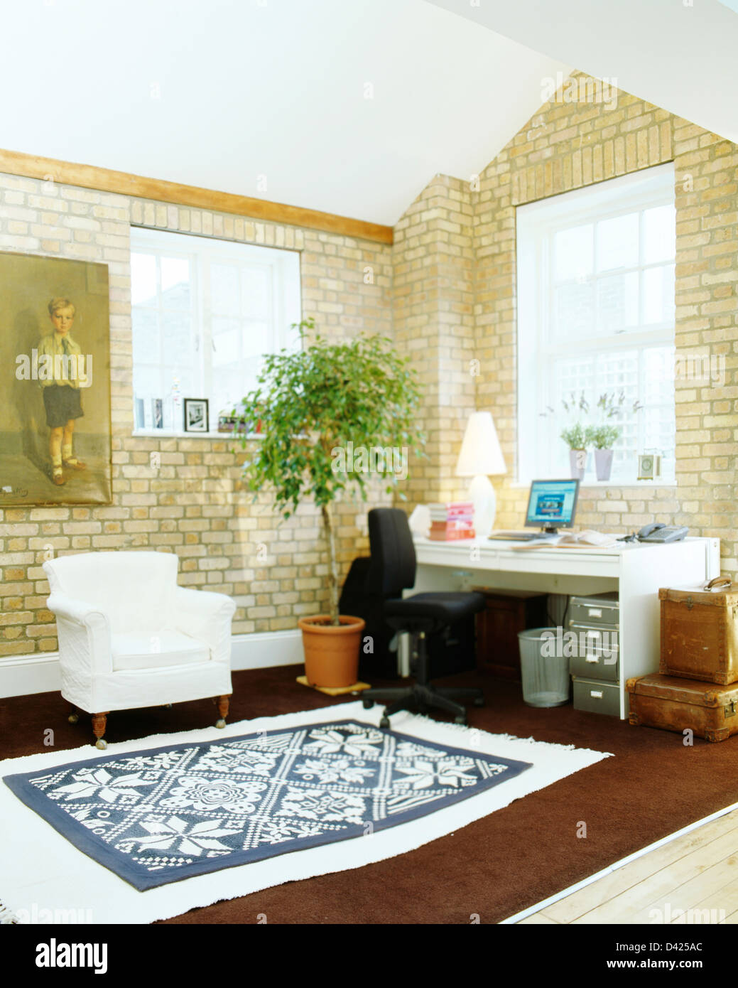 Fauteuil blanc et bleu tapis et pot avec petit arbre en bureau à domicile en fabrique de piano converti avec grande peinture sur mur de brique Banque D'Images