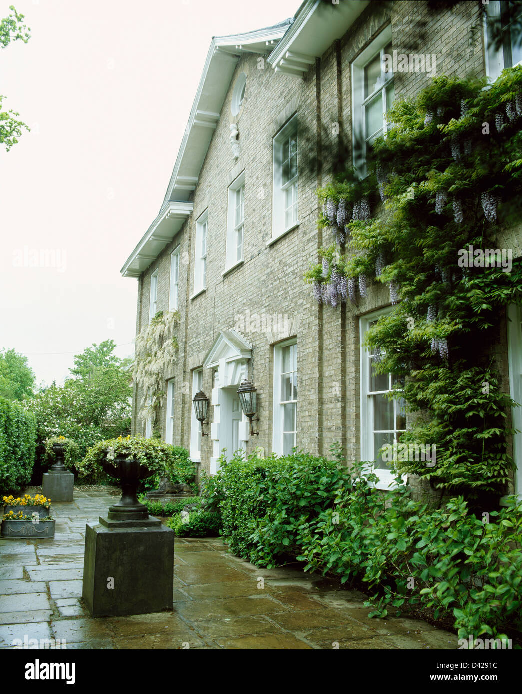 Urne sur socle sur une terrasse pavée en face de grande maison de campagne avec glycine mauve sur les murs Banque D'Images