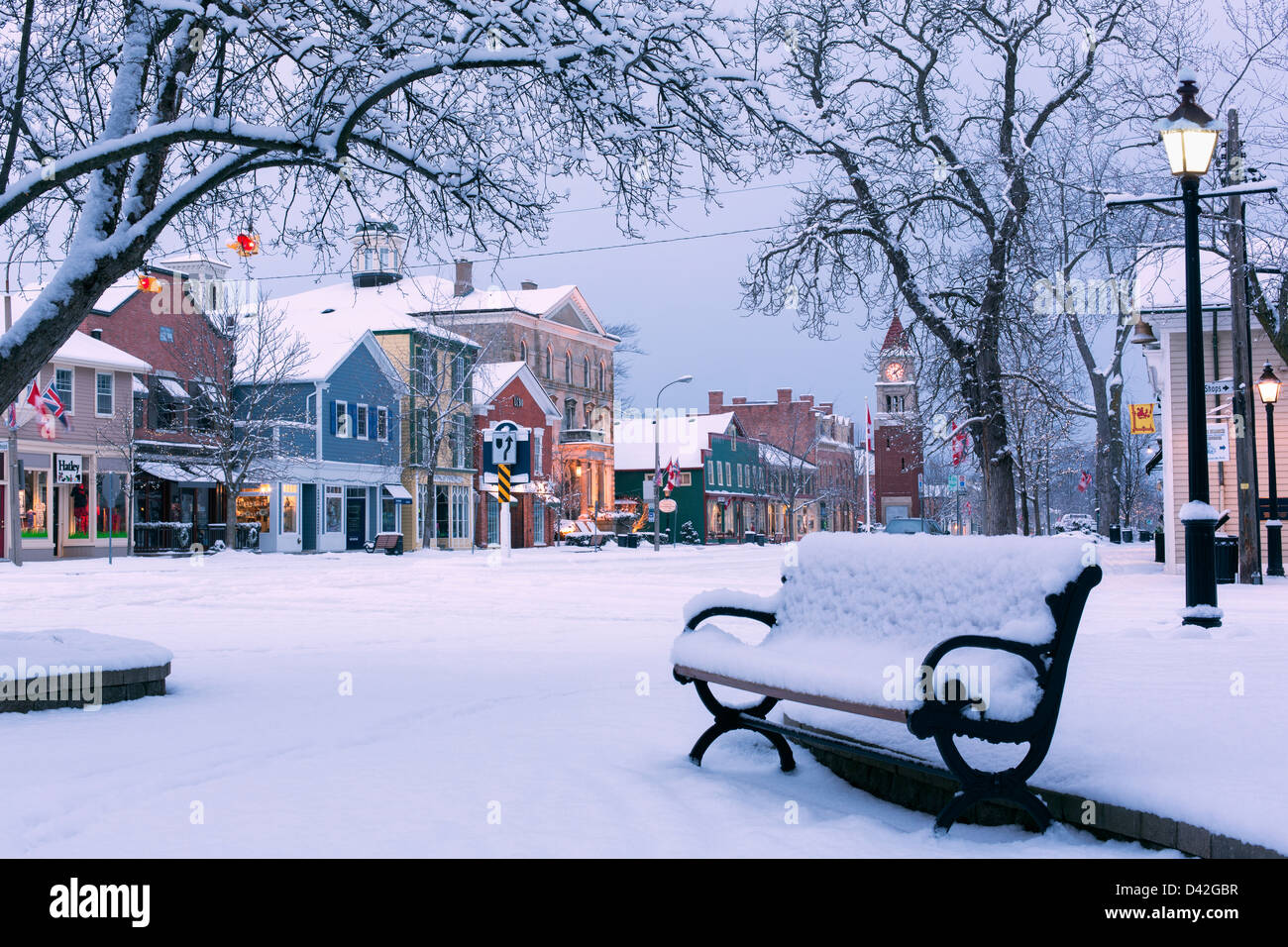 Canada, Ontario, Niagara-on-the-Lake, rue Queen, matin du début de l'hiver,banc de parc couvert de neige montrant une rue principale avec des boutiques. Banque D'Images