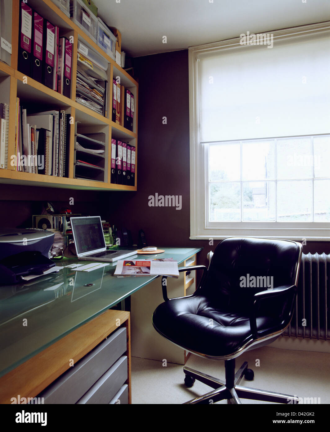 Fauteuil pivotant en cuir noir recouvert de verre au bureau avec un ordinateur portable dans l'étude avec fort fichiers sur tablettes murales Banque D'Images