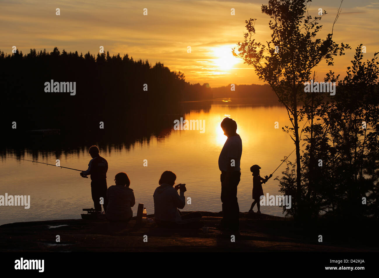 Silvkoparen, Suède, une famille s'assied sur le bord d'un lac au coucher du soleil Banque D'Images