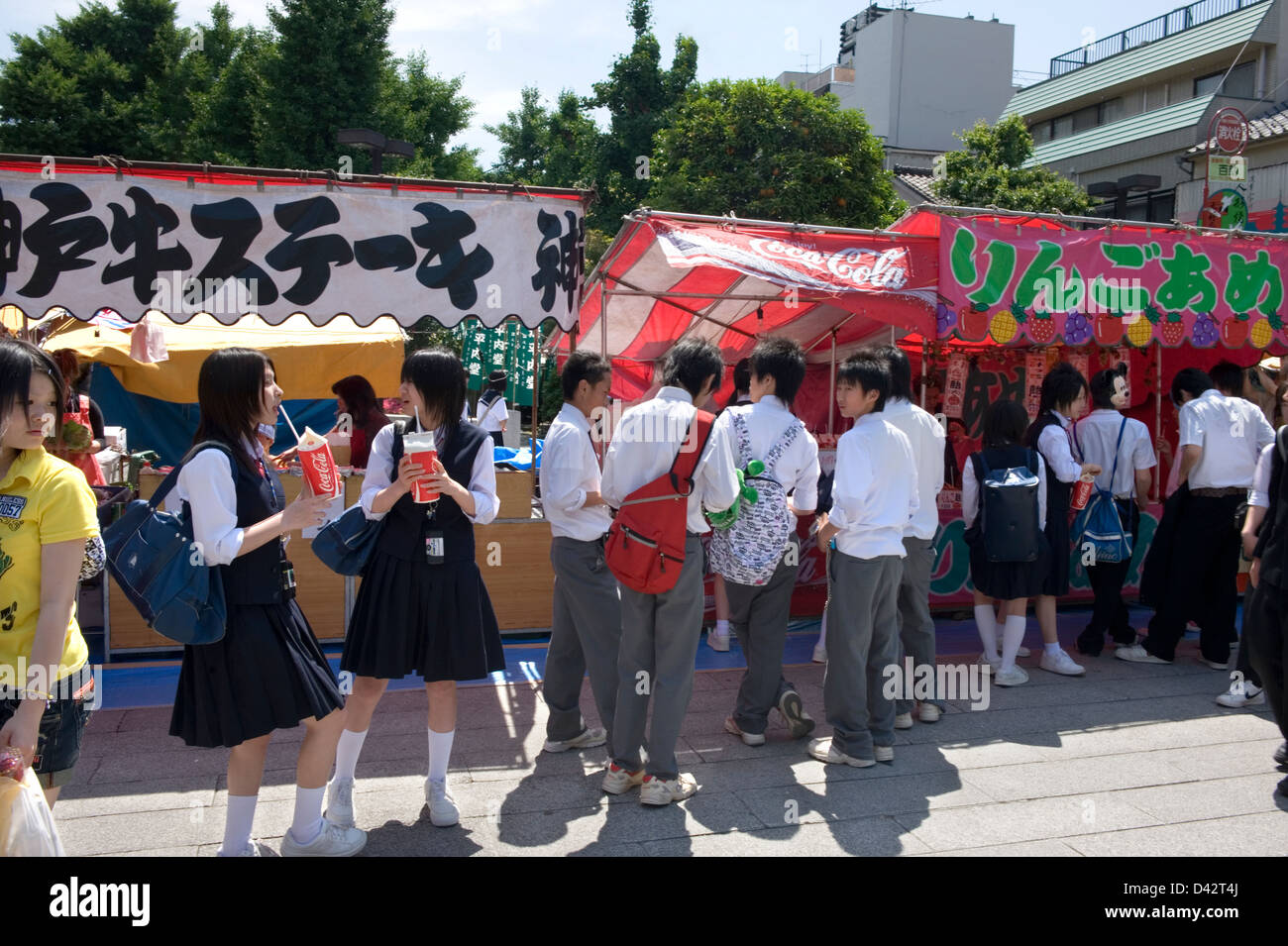 Les jeunes filles du secondaire et les garçons en uniforme profitez de l'atmosphère de fête tout en flânant autour de roten stands jeux et collations Banque D'Images