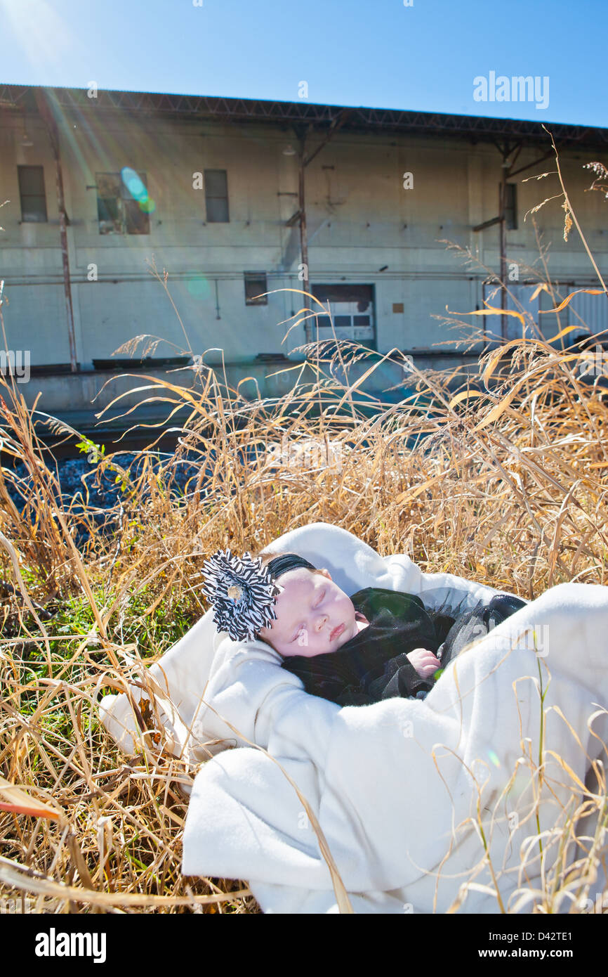 Une petite fille bébé dormir dans un panier dans les hautes herbes avec les rayons du soleil. Banque D'Images