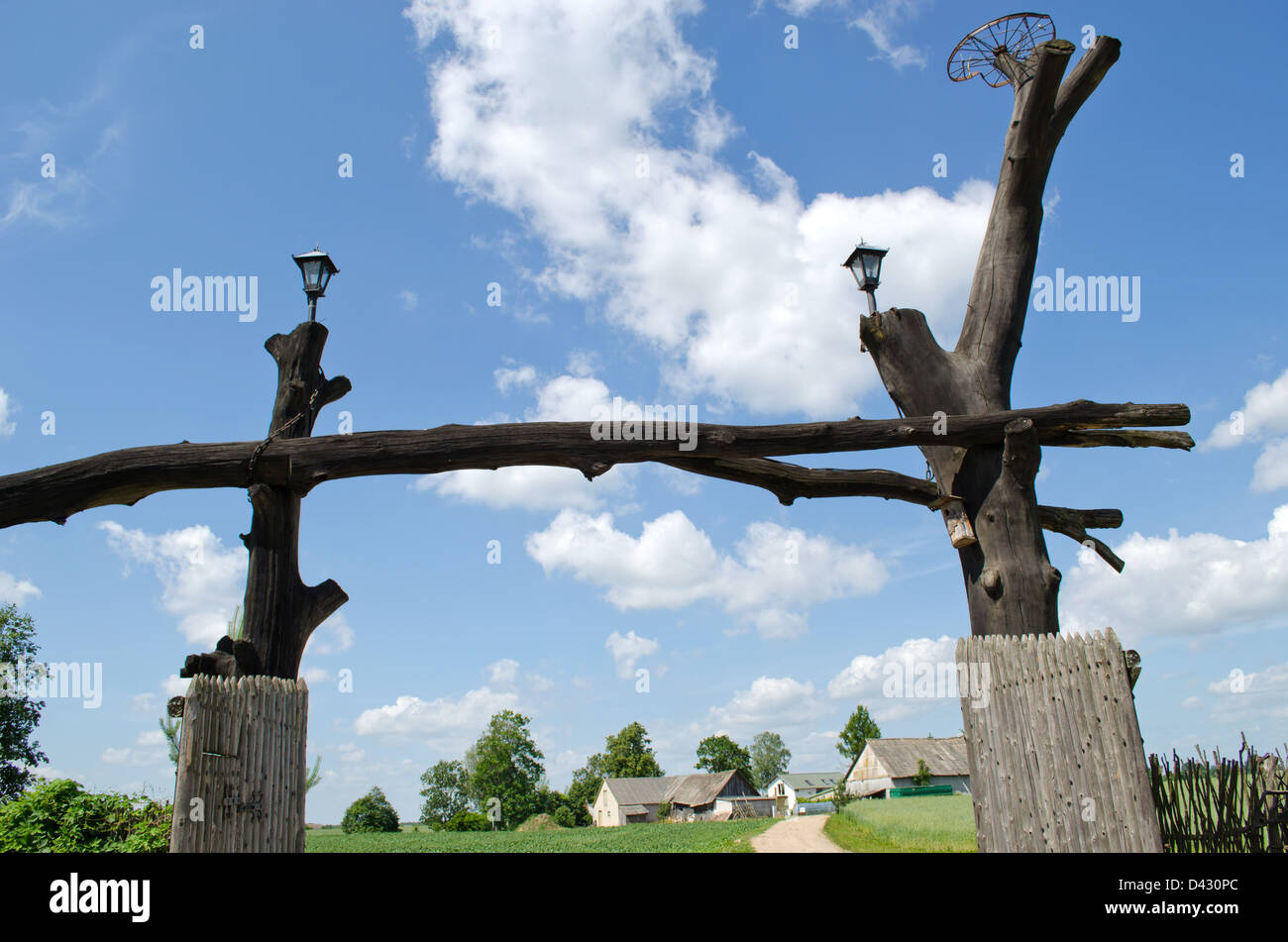 Parc en bois gate fait de vieux troncs d'arbres et maisons rurales homestead sur bleu ciel nuageux. Banque D'Images