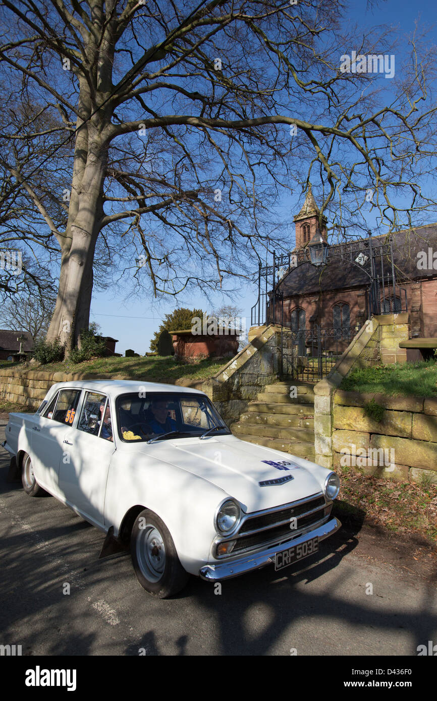 Village de Coddington, Angleterre. Vue pittoresque sur un livre blanc 1967 Mk1 Ford Cortina GT en passant par le village de Coddington. Banque D'Images