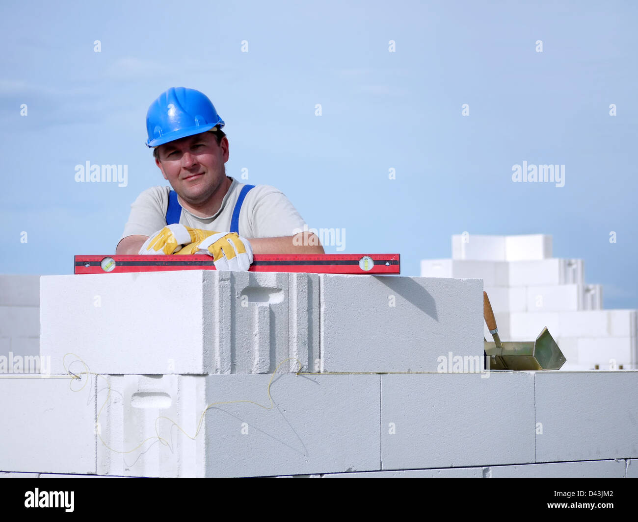 Mason portant des casques bleus posant reposant sur un mur de bloc blanc sur ciel bleu Banque D'Images