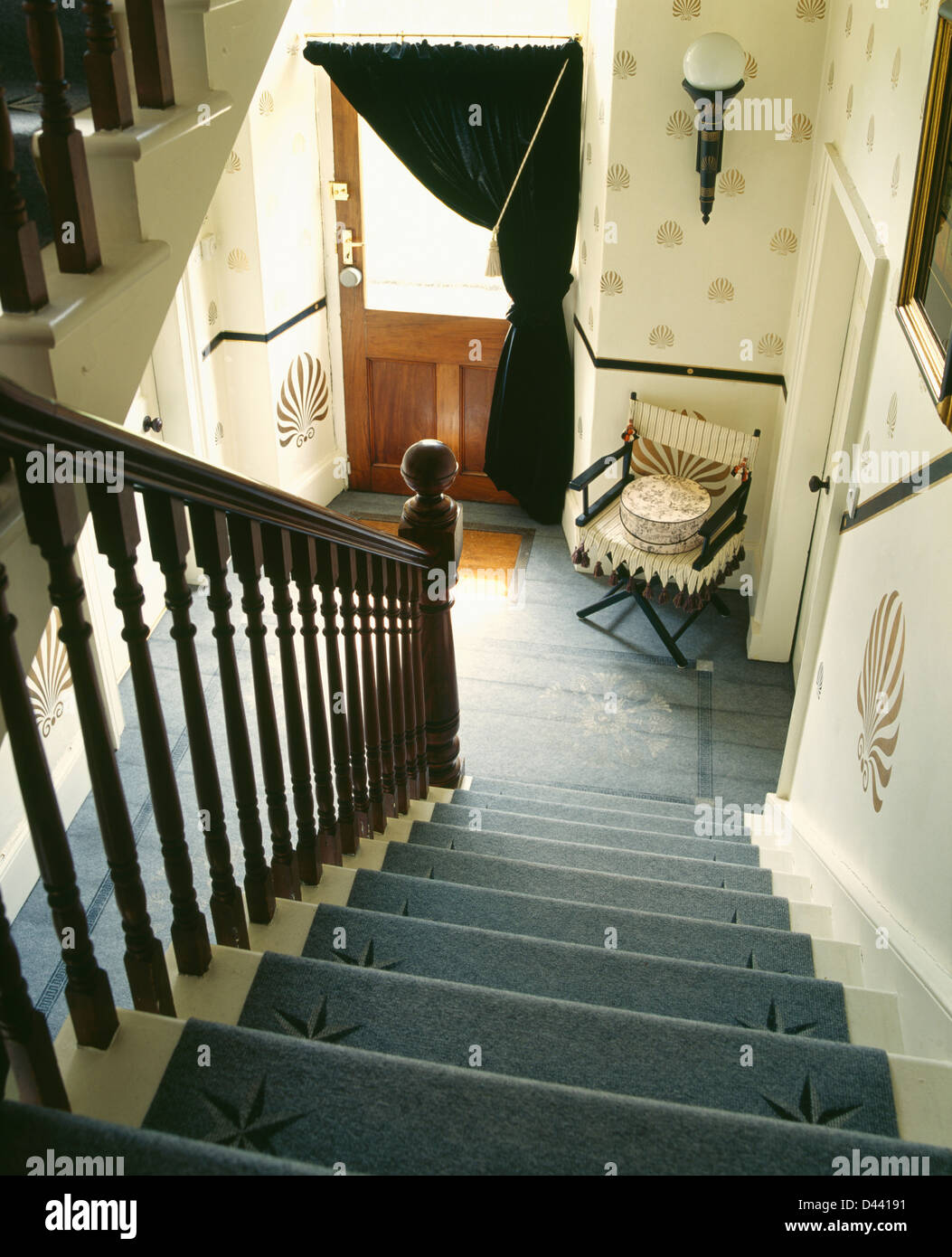 Tapis gris au pochoir sur l'escalier dans le hall avec des murs au pochoir et fauteuil à côté de porte d'entrée avec le rideau de velours Banque D'Images