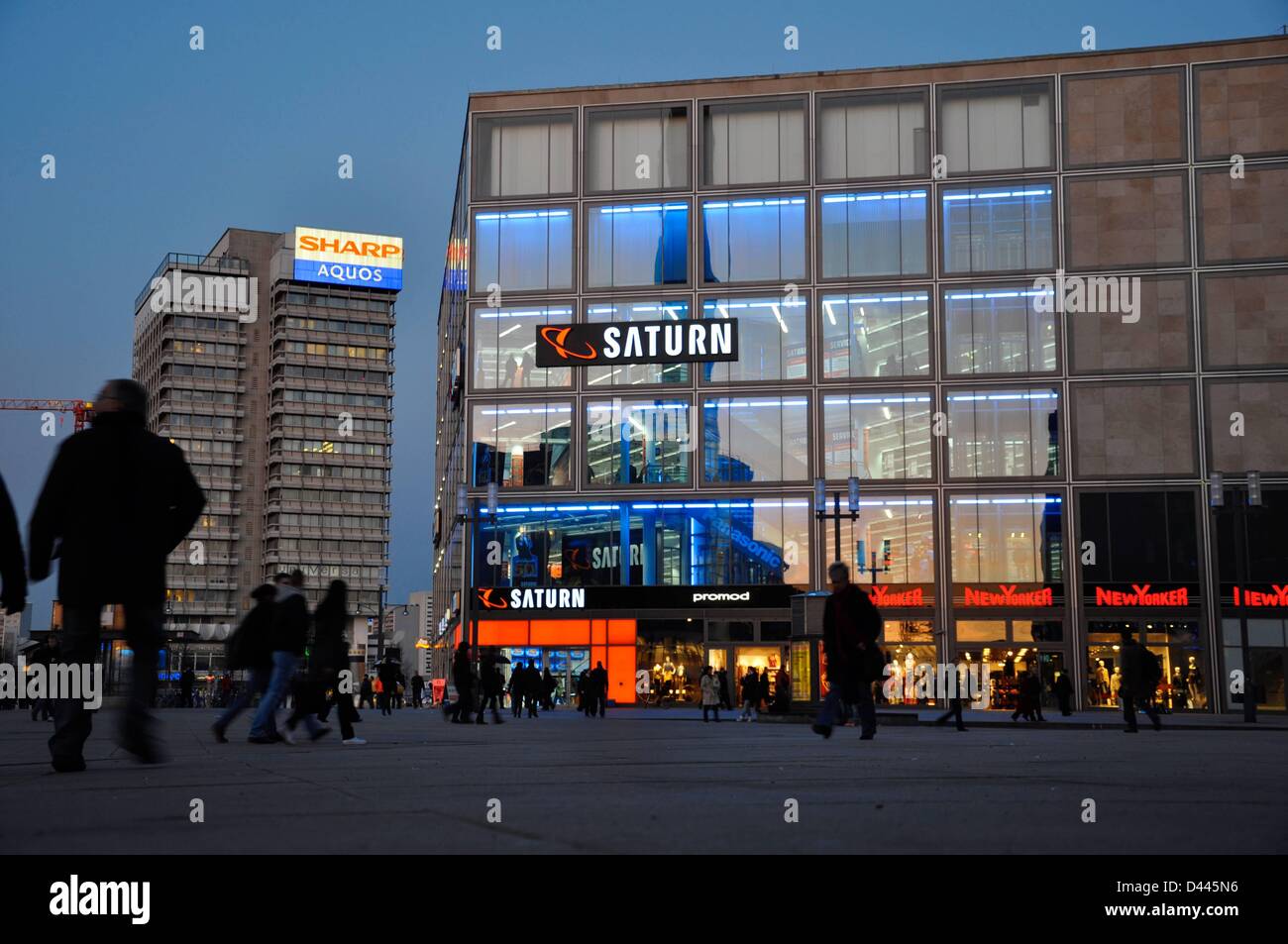 Des gens marchent devant une succursale du détaillant d'électronique grand public Saturn à Alexanderplatz à Berlin, Allemagne, le 7 mars 2011. En arrière-plan, la Haus des Reisens (Maison du voyage) est photographiée avec l'écriture au néon 'Sharp Aquos'. Pendant l'ère GDR, le bâtiment abritait l'agent de voyage GDR 'Interflug'. Fotoarchiv für ZeitgeschichteS.Steinach Banque D'Images