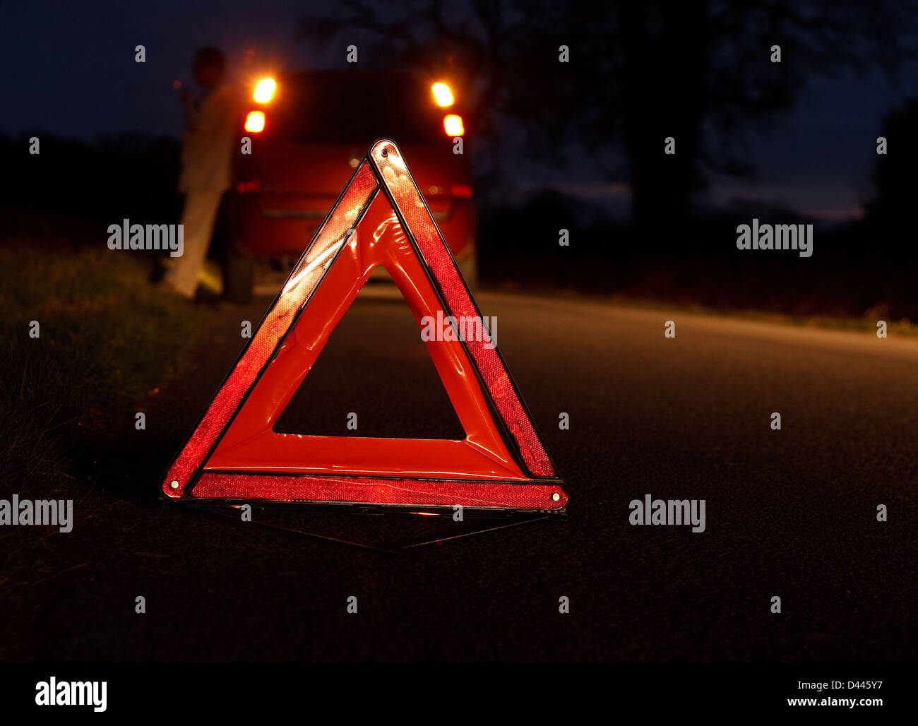 Voiture chauffeur récupération attend après avoir connu une panne de véhicule dans la nuit avec un triangle d'avertissement Banque D'Images