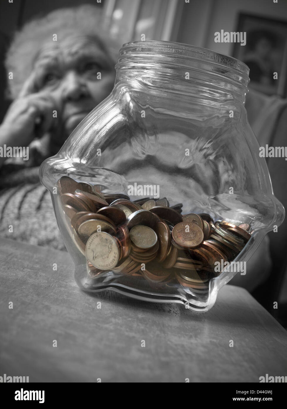 INFLATION LE POT D'ÉPARGNE DES PERSONNES ÂGÉES inquiétait une femme âgée et vulnérable dans son salon avec un pot d'épargne des espèces sur la table B&W/Color Banque D'Images