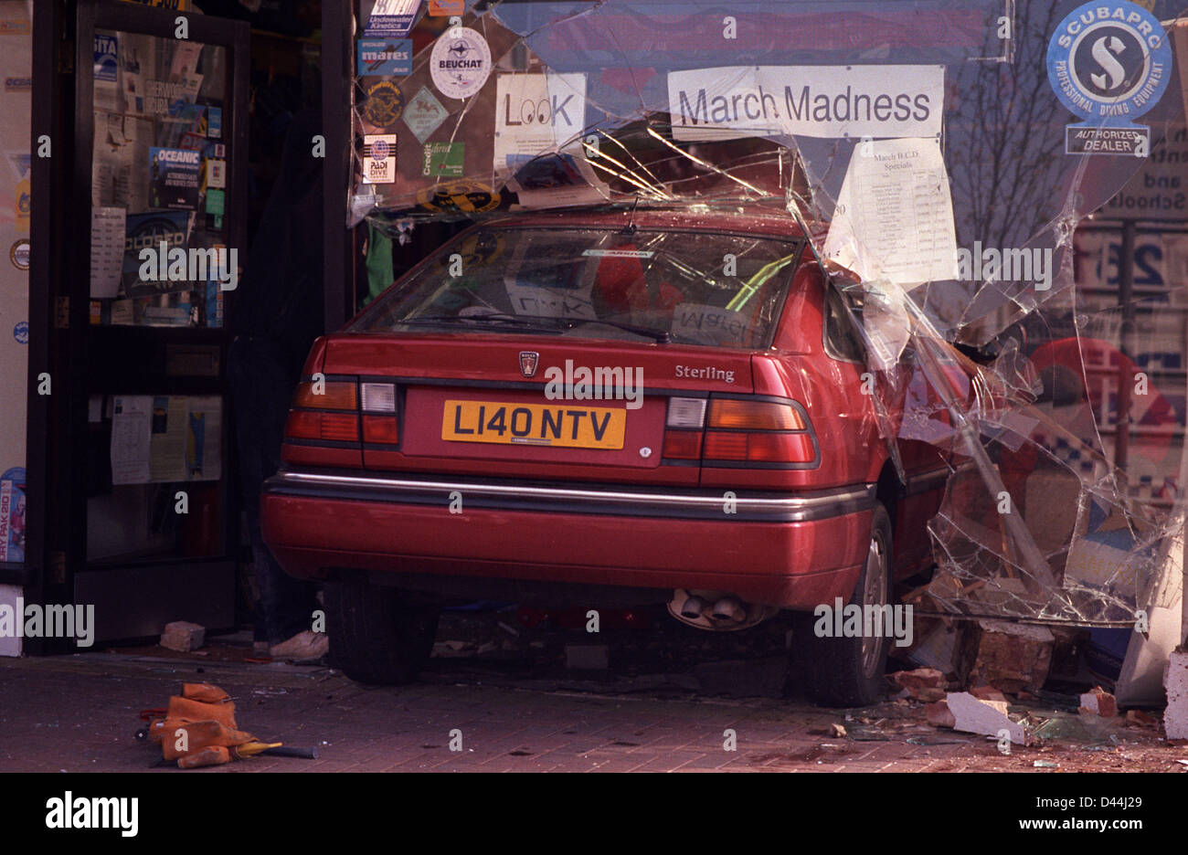 Une voiture rouge s'est écrasé accidentellement par un sous aqua shop window s'immobiliser au-dessous d'un 'March Madness' vente. Banque D'Images