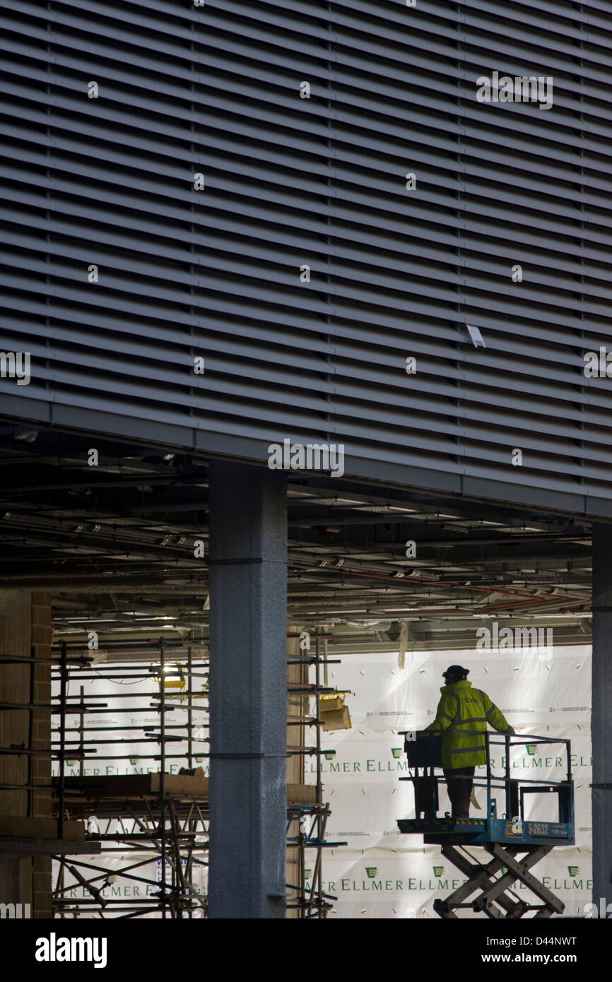 Un ouvrier qui exploite une plateforme élévatrice cailing sous la grande d'un nouveau développement dans Fenbchurch Street au coeur de la capitale, le quartier financier. Entouré par les échafaudages et les draps à proximité d'un chantier de façade, l'homme inspecte les travaux menés par d'autres personnes de la sécurité et de la hauteur de la plateforme élévatrice. Banque D'Images