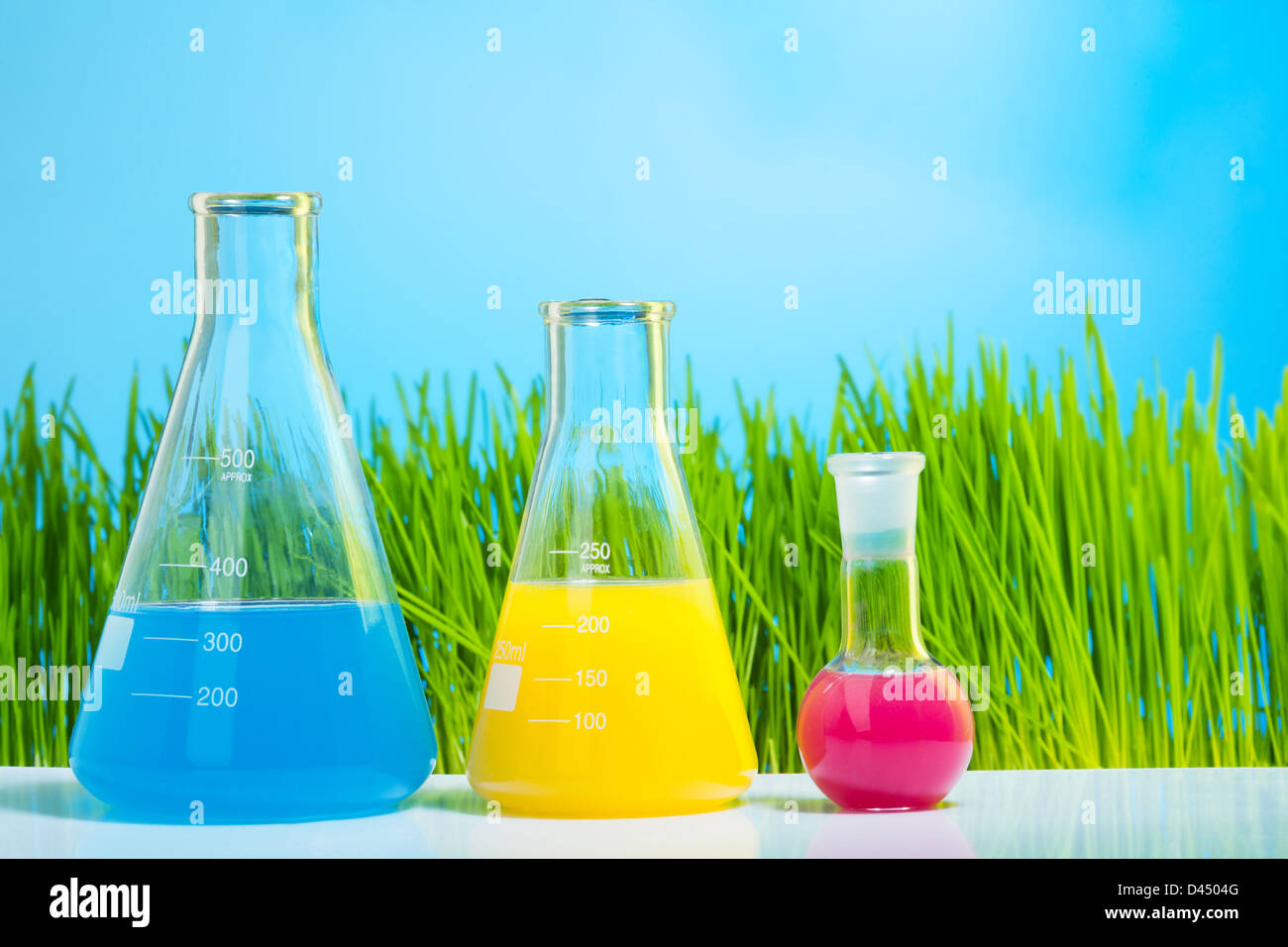 Tubes et flacons de laboratoire colorés avec de l'herbe fraîche du printemps sur fond vert clair Banque D'Images