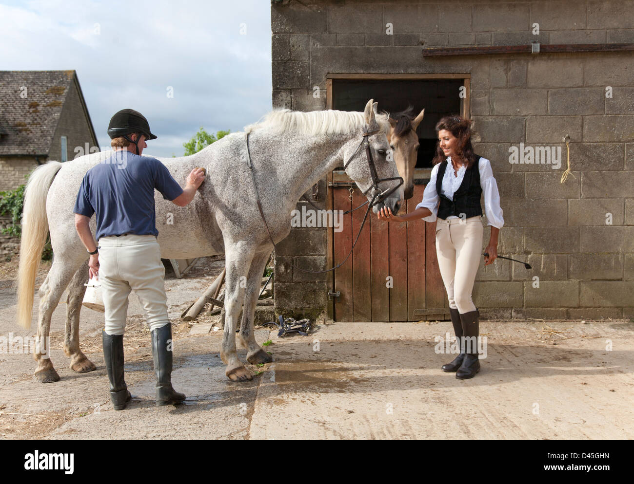 Un homme et femme en équipement d'équitation palefrenier et caresser un cheval dans une cour stable de Cotswold Banque D'Images