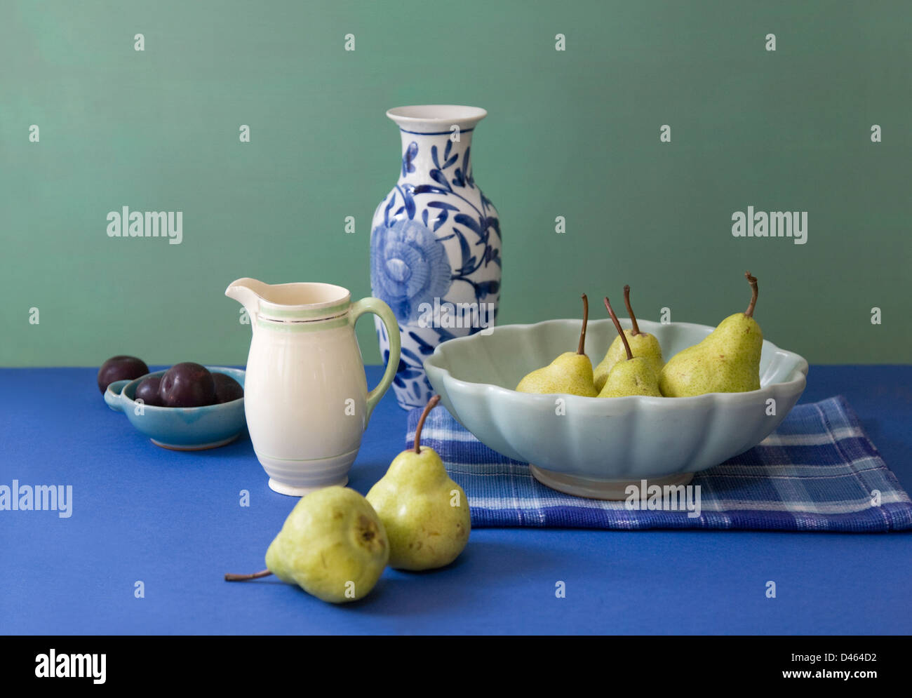 De couleur coordonnée de la vie toujours de la vaisselle, des poires et prunes sur un tableau bleu avec un fond vert Banque D'Images