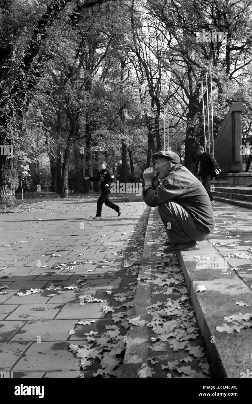 Vieux homme accroupi sur les mesures, le parc Panfilov, Almaty, Kazakhstan Banque D'Images