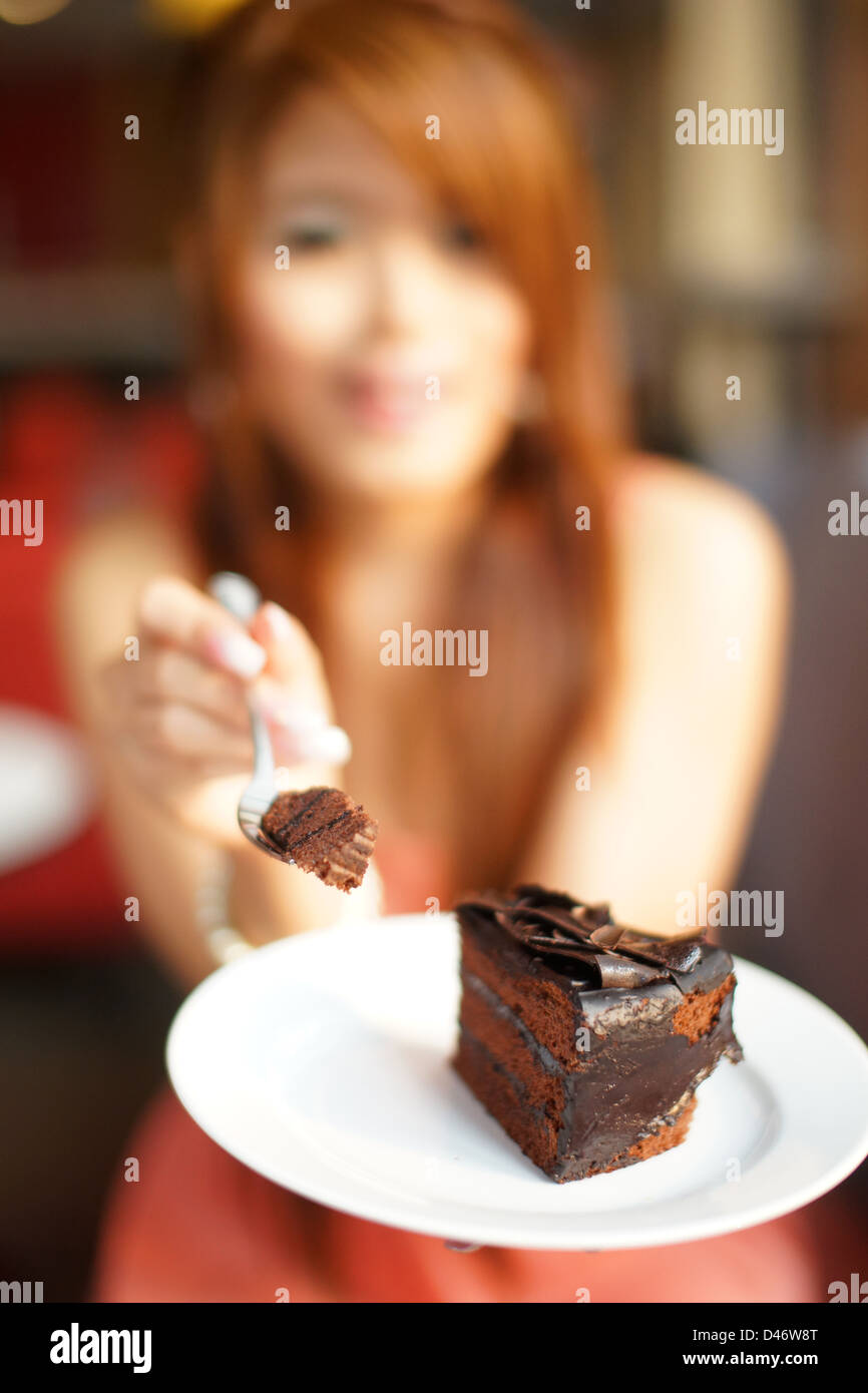 Young Beautiful woman sitting in cafe de manger un gâteau au chocolat. L'accent sur le gâteau. Banque D'Images